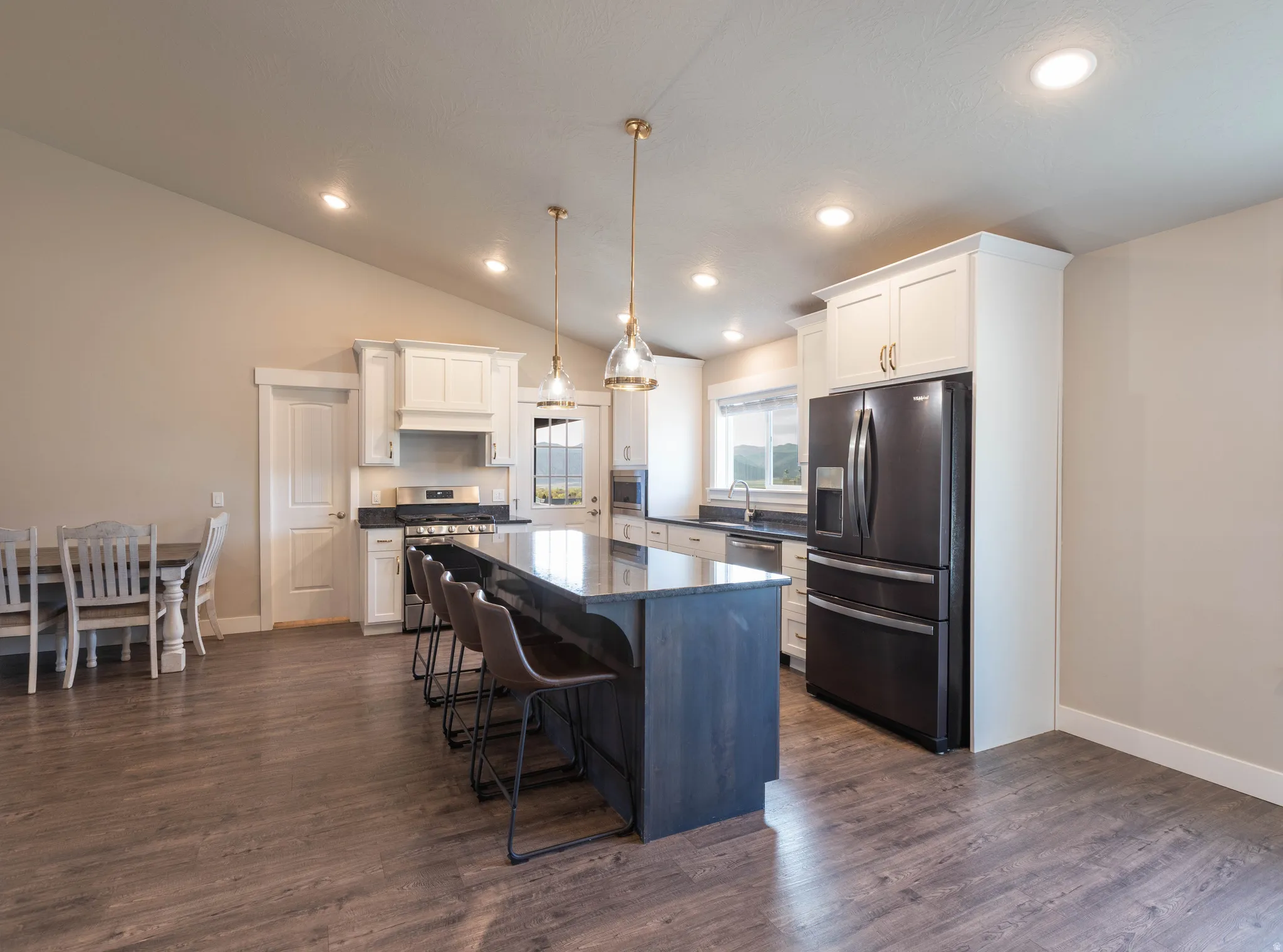 Kitchen with stainless steel appliances, a kitchen breakfast bar, dark wood-style flooring, a kitchen island, and vaulted ceiling