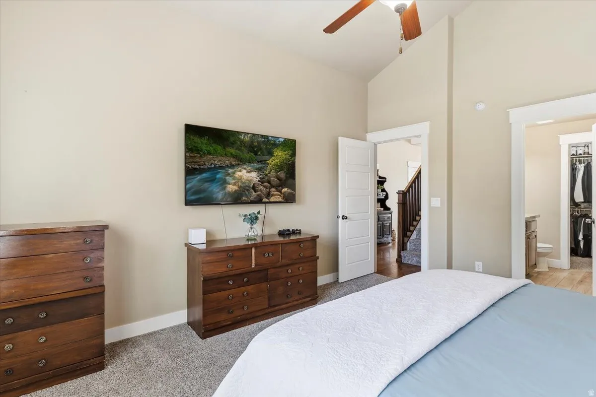 Primary Bedroom with lofted ceiling, light carpet, ensuite bath, and a ceiling fan