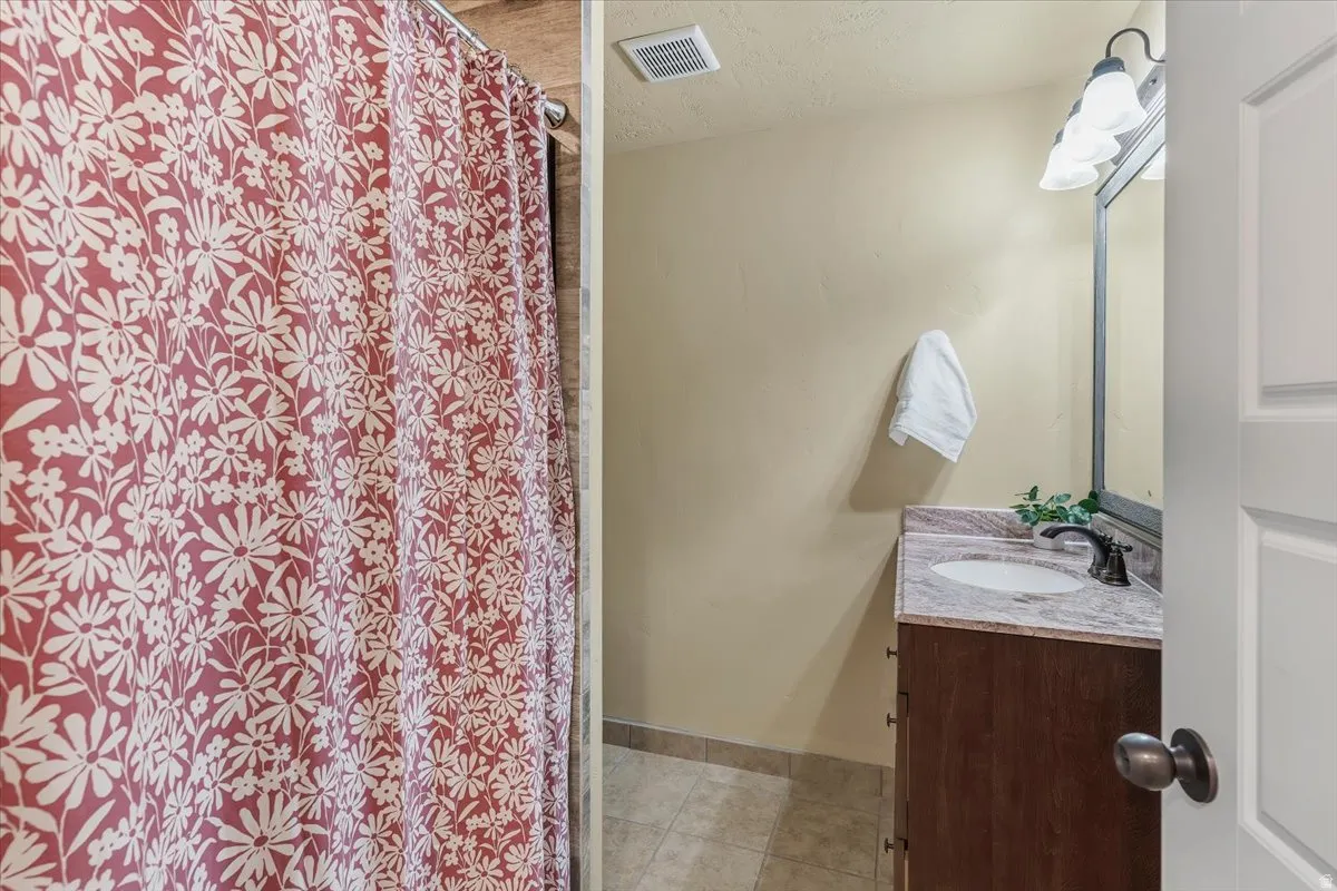 Bathroom featuring vanity, a shower with curtain, light tile patterned flooring, and a textured ceiling
