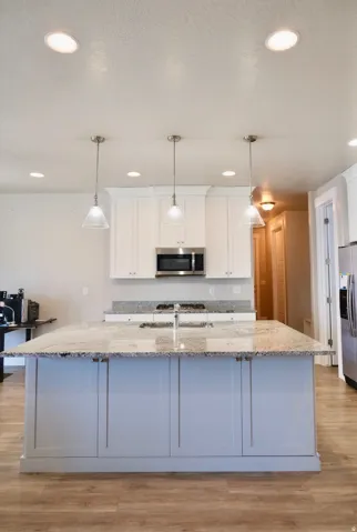 Kitchen with white cabinets, light stone counters, light LVP wood-style flooring, and a large island with sink