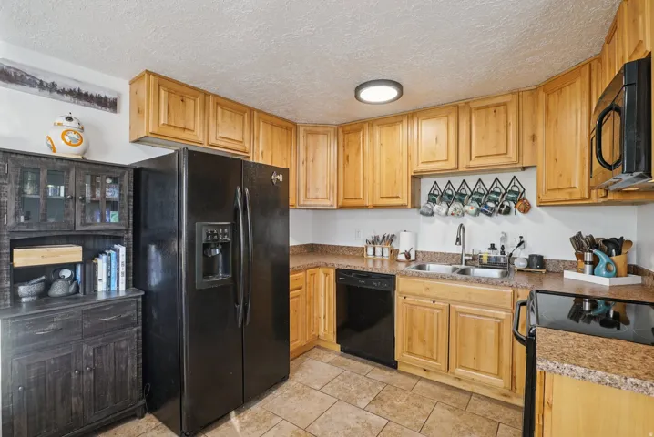 Kitchen with black appliances, a textured ceiling, light wood finish cabinetry, and light countertops