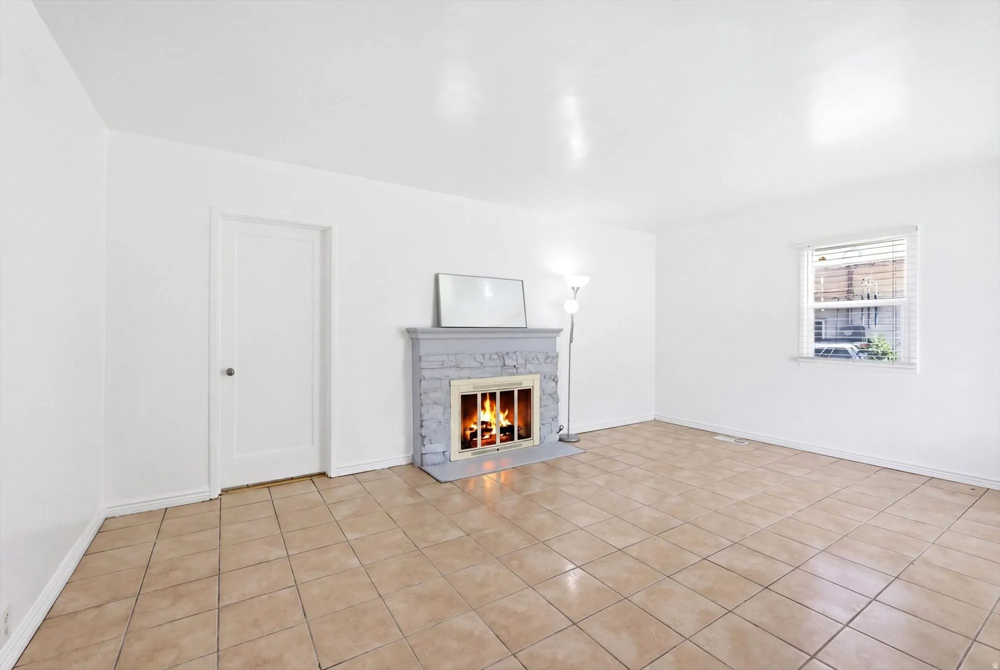 Unfurnished living room featuring a warm lit fireplace and light tile patterned floors