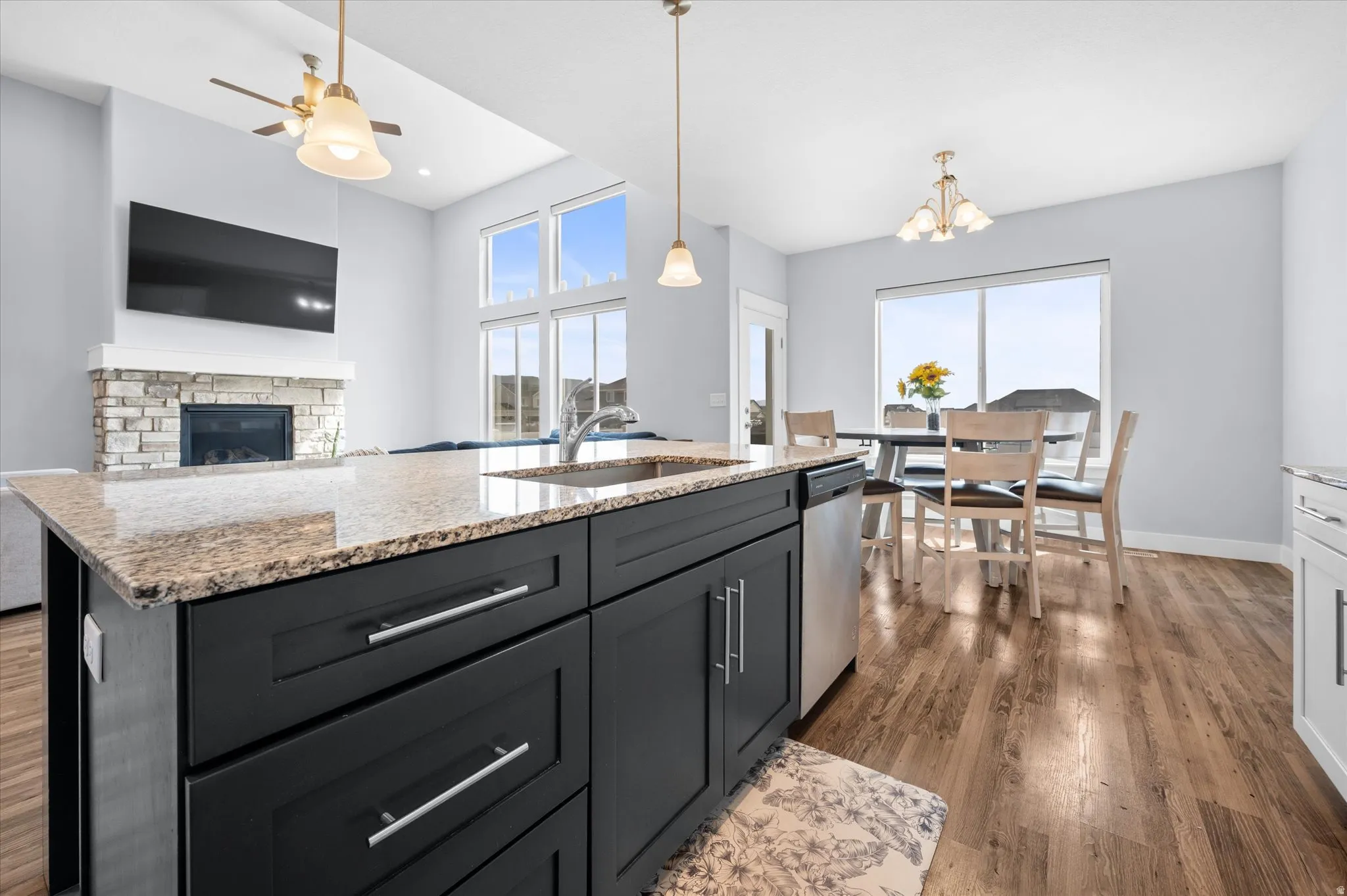 Kitchen with a fireplace, light stone countertops, dark wood finished floors, and a kitchen island with sink