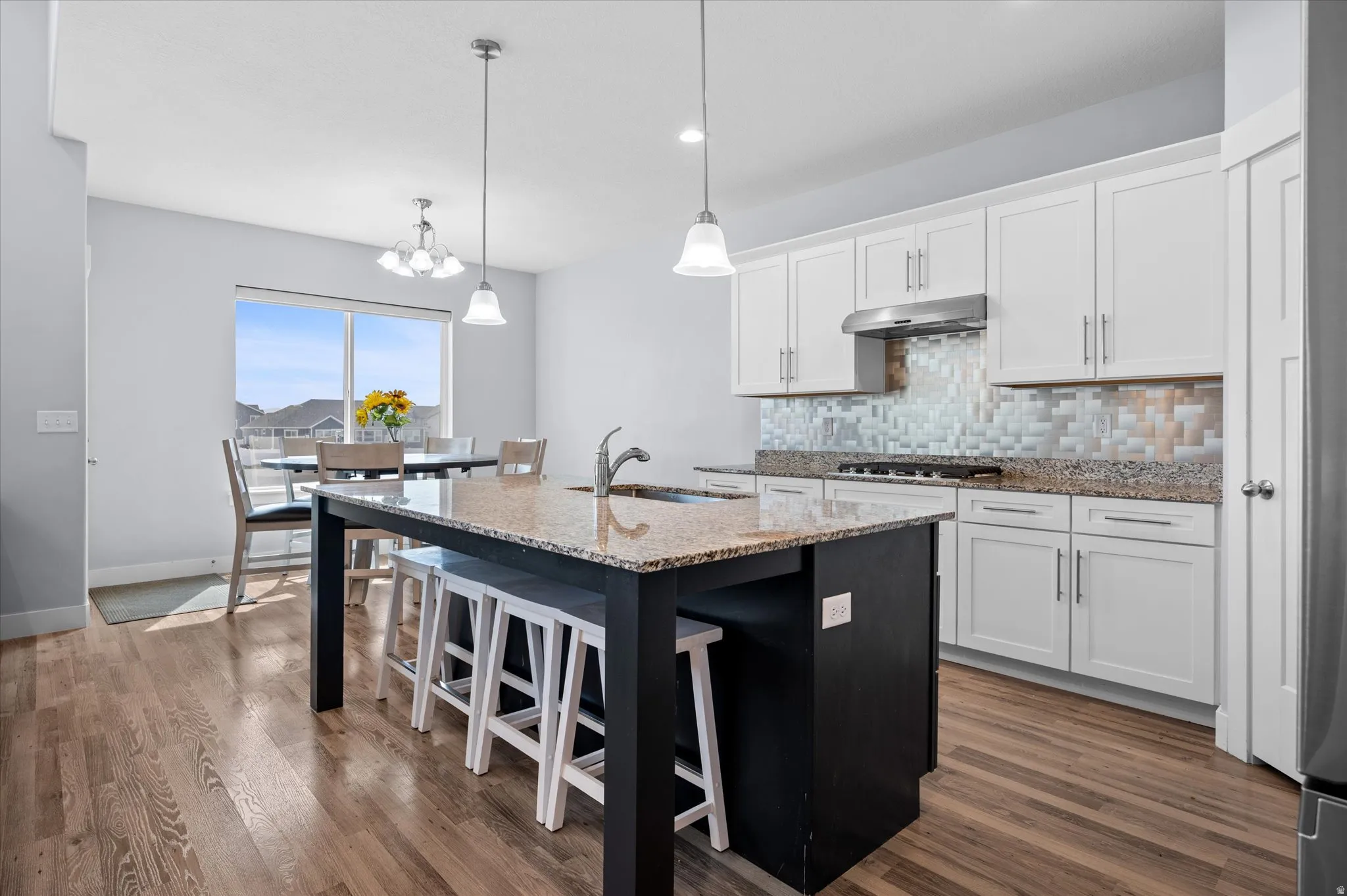Dual tone kitchen with a breakfast bar area, light stone counters, a center island with sink, decorative backsplash, and dark wood-style floors