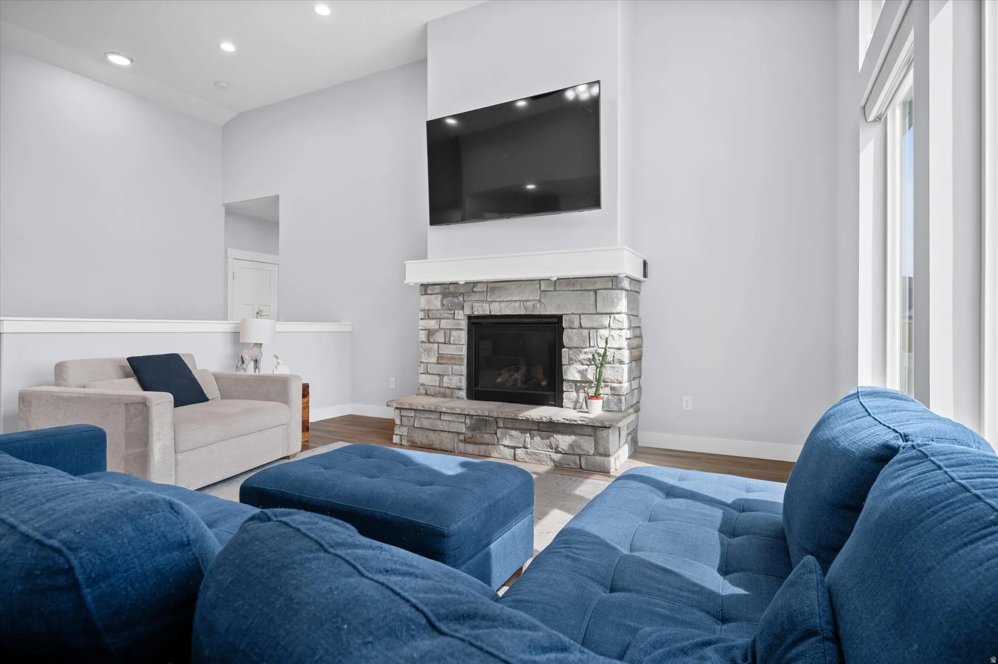 Living room featuring wood finished floors, a cathedral ceiling, a stone fireplace, and recessed lighting