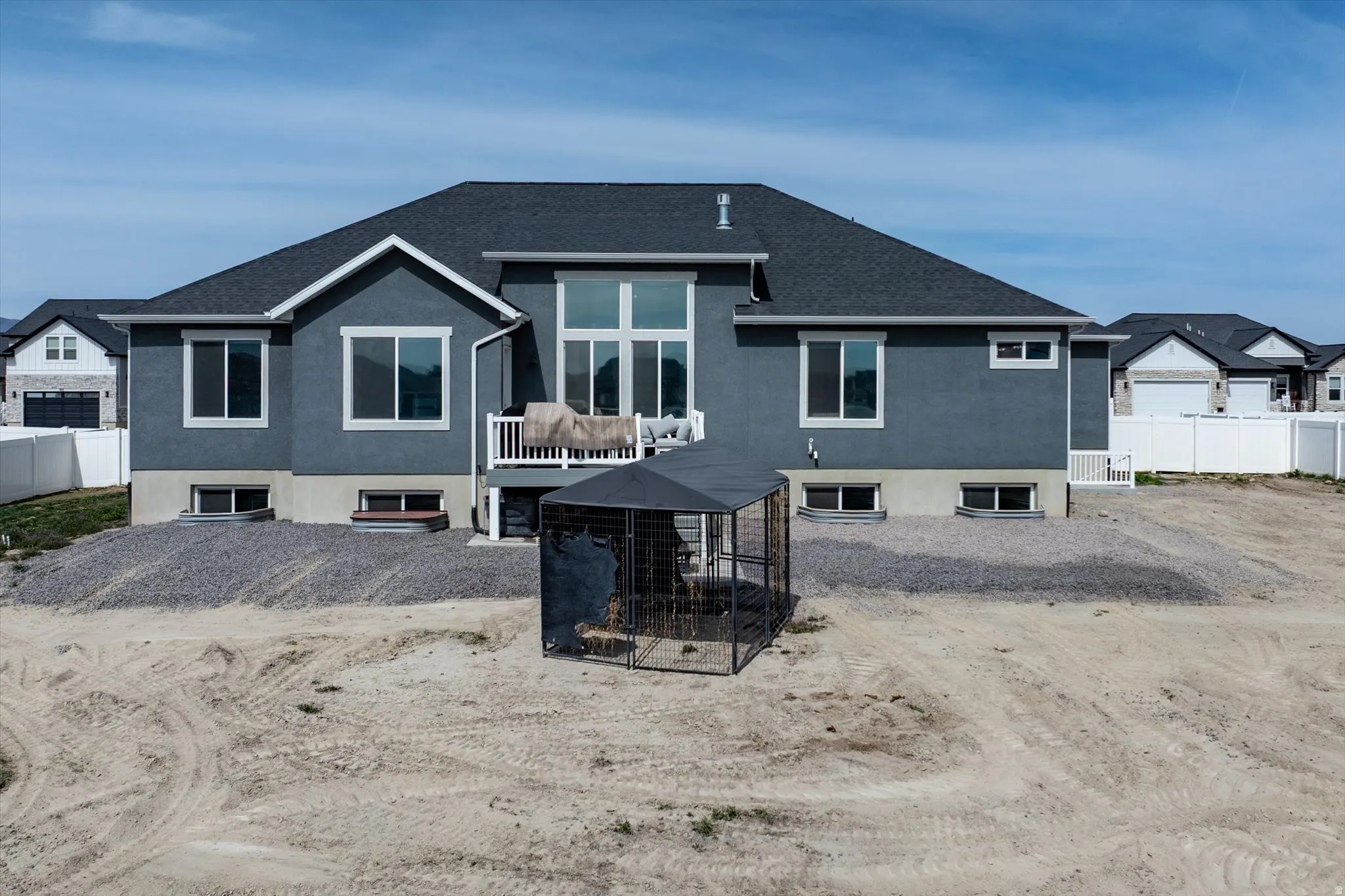 Back of property with stucco siding, a shingled roof, showing the cathedral ceiling and extra height family room area, an outbuilding, and a deck
