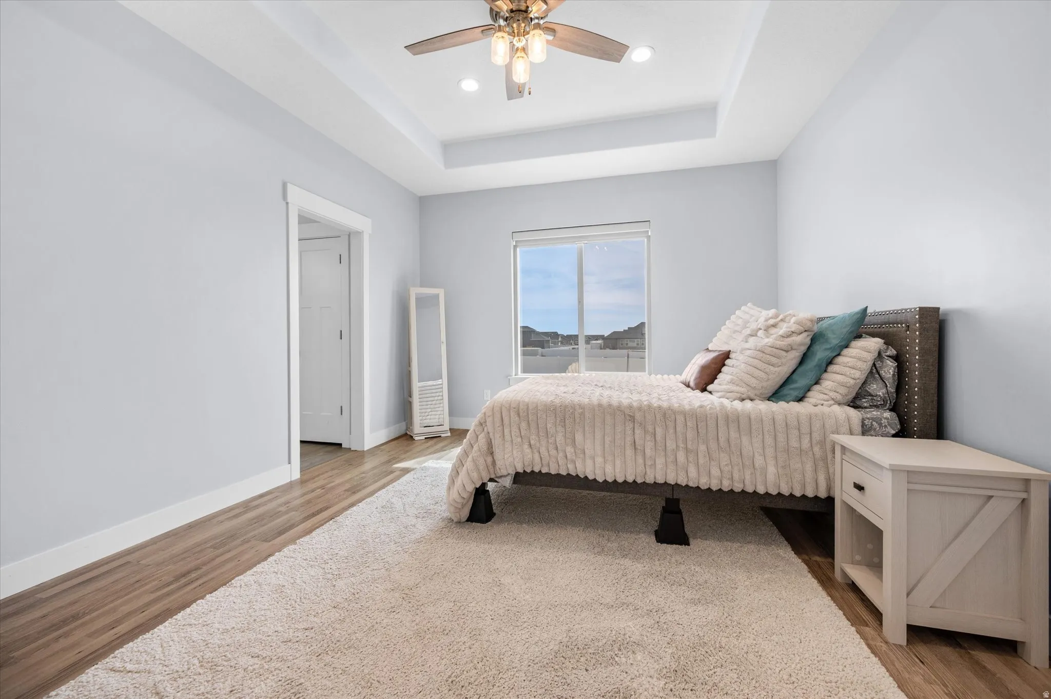Owners suite with light wood-style floors, a raised ceiling, ceiling fan, and upgraded recessed lighting