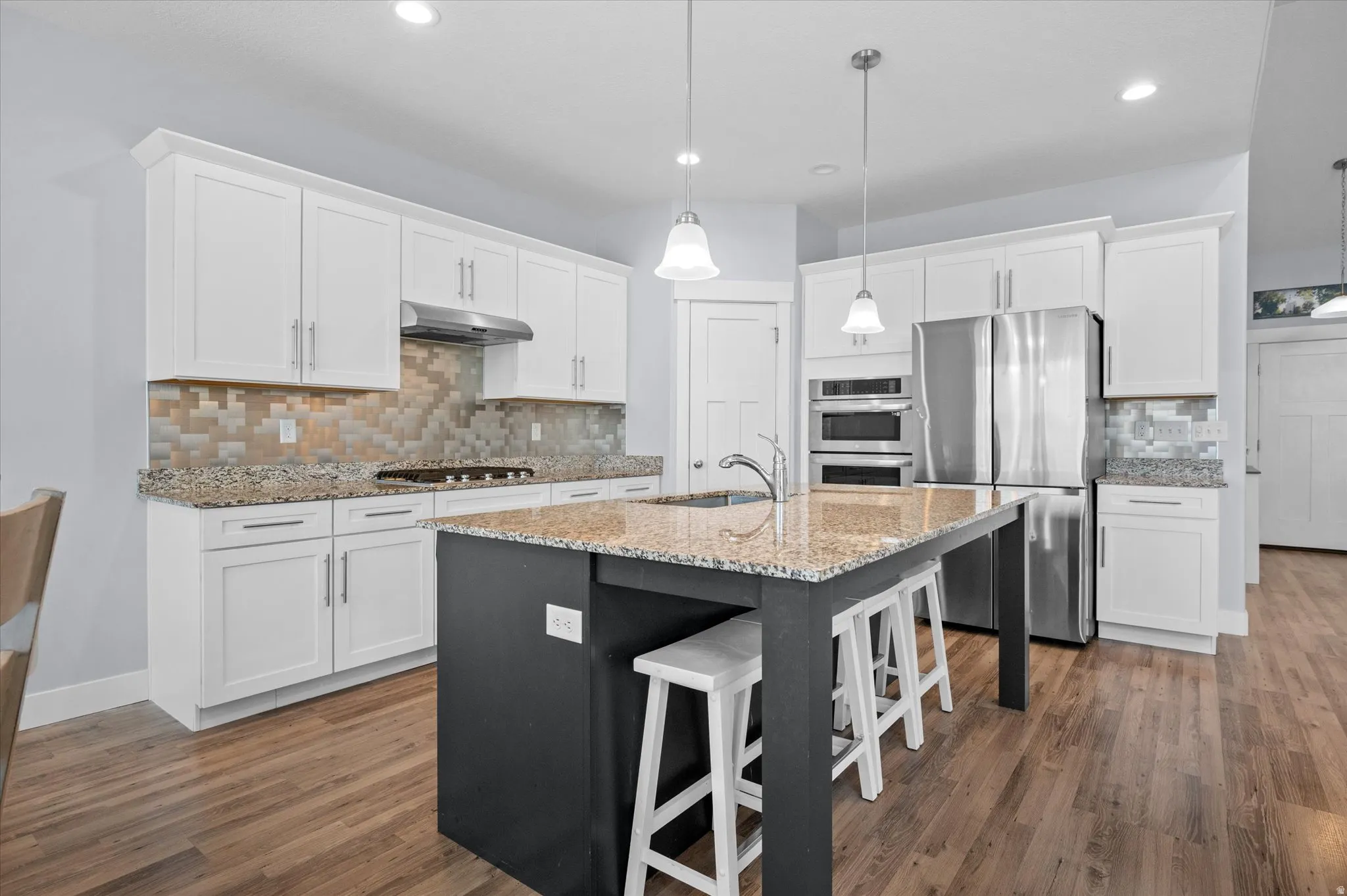 Dual tone kitchen with light stone countertops, a kitchen breakfast bar, stainless steel appliances, gas stove, wall ovens, wall microwave, a center island with sink, and dark wood-type flooring