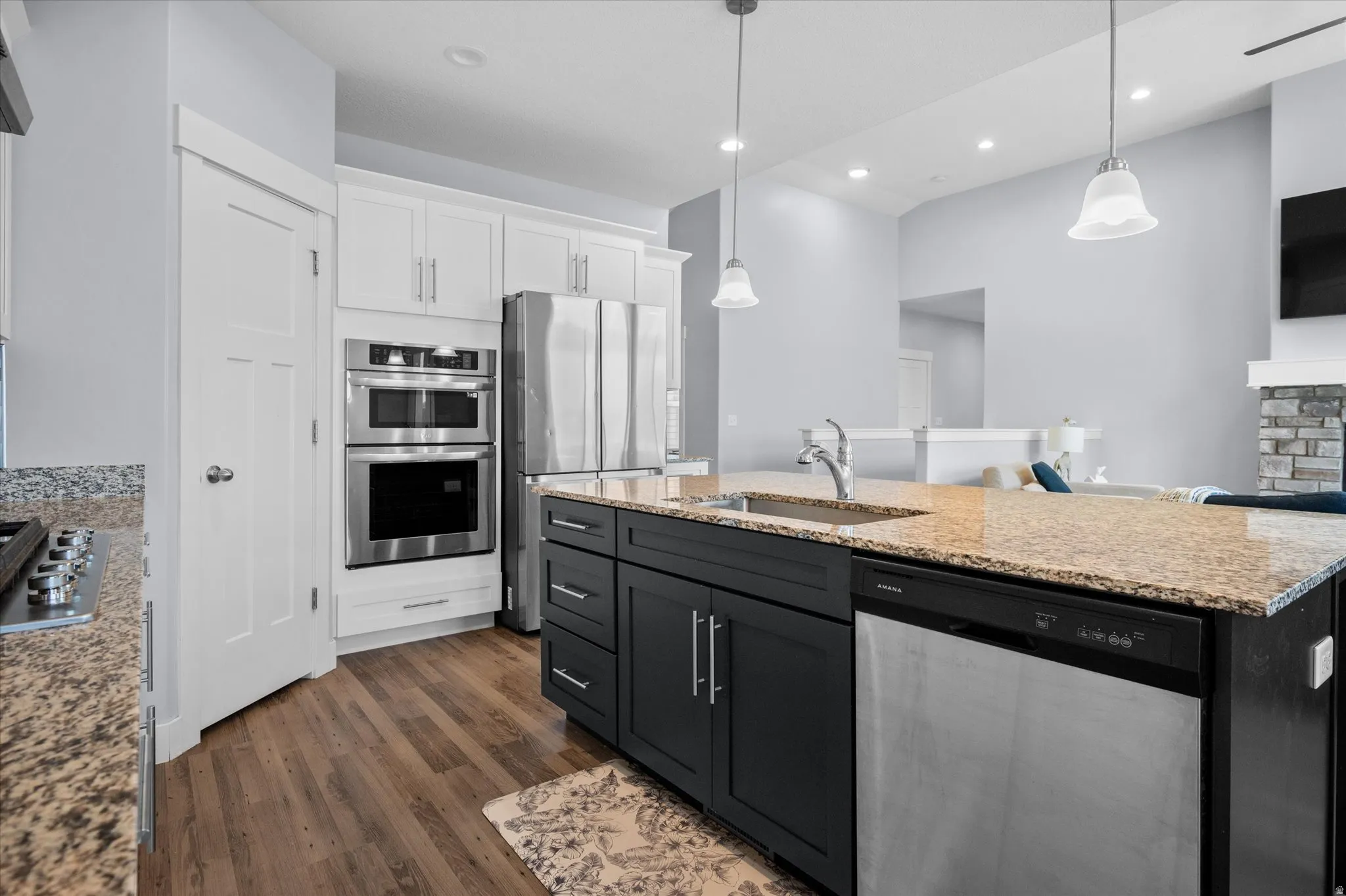 Kitchen with stainless steel appliances, two tone cabinetry, a center island with sink, light stone counters, and dark wood-type flooring