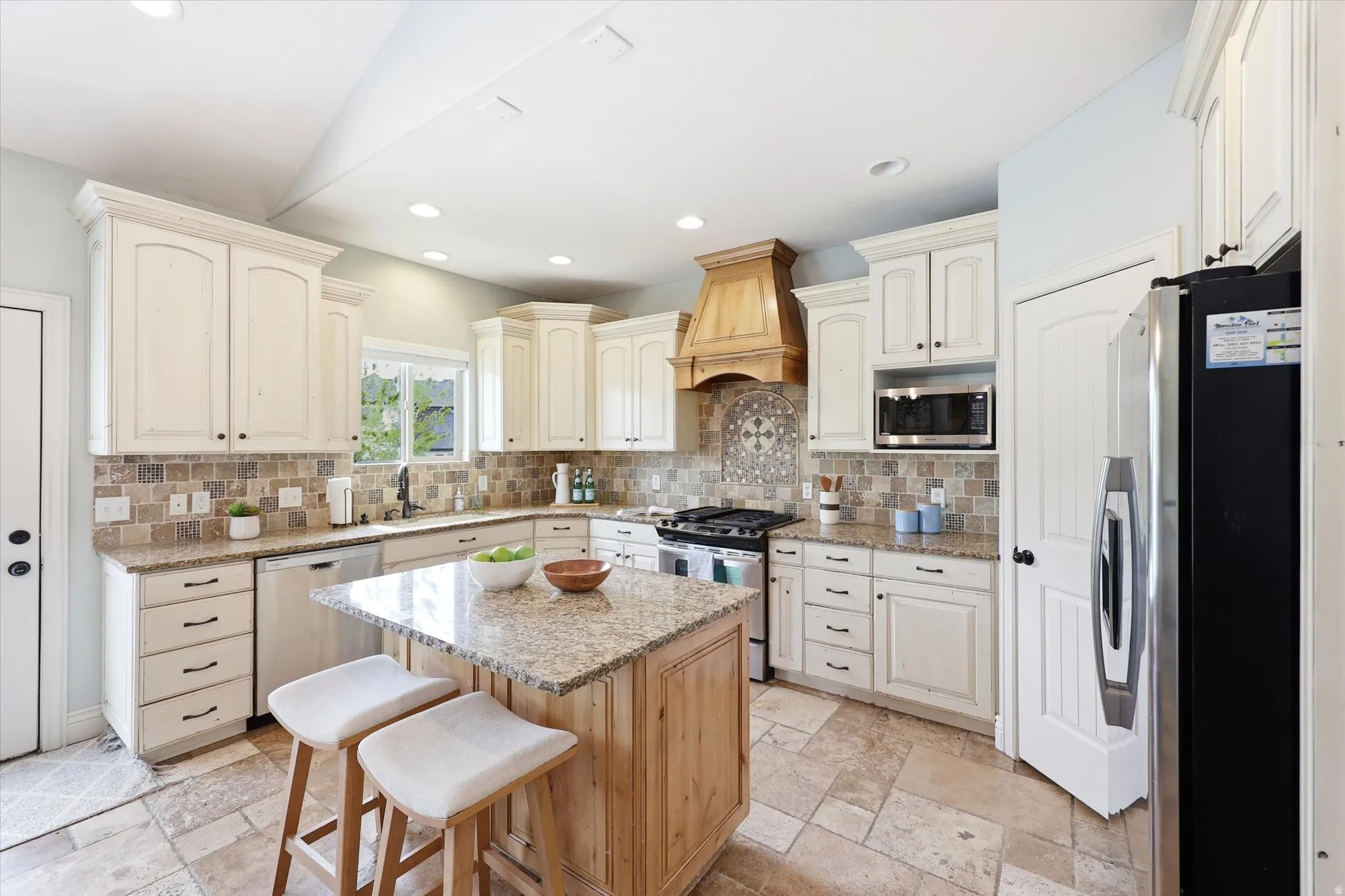 Kitchen with stainless steel appliances, light stone counters, a kitchen breakfast bar, decorative backsplash, and stone tile floors