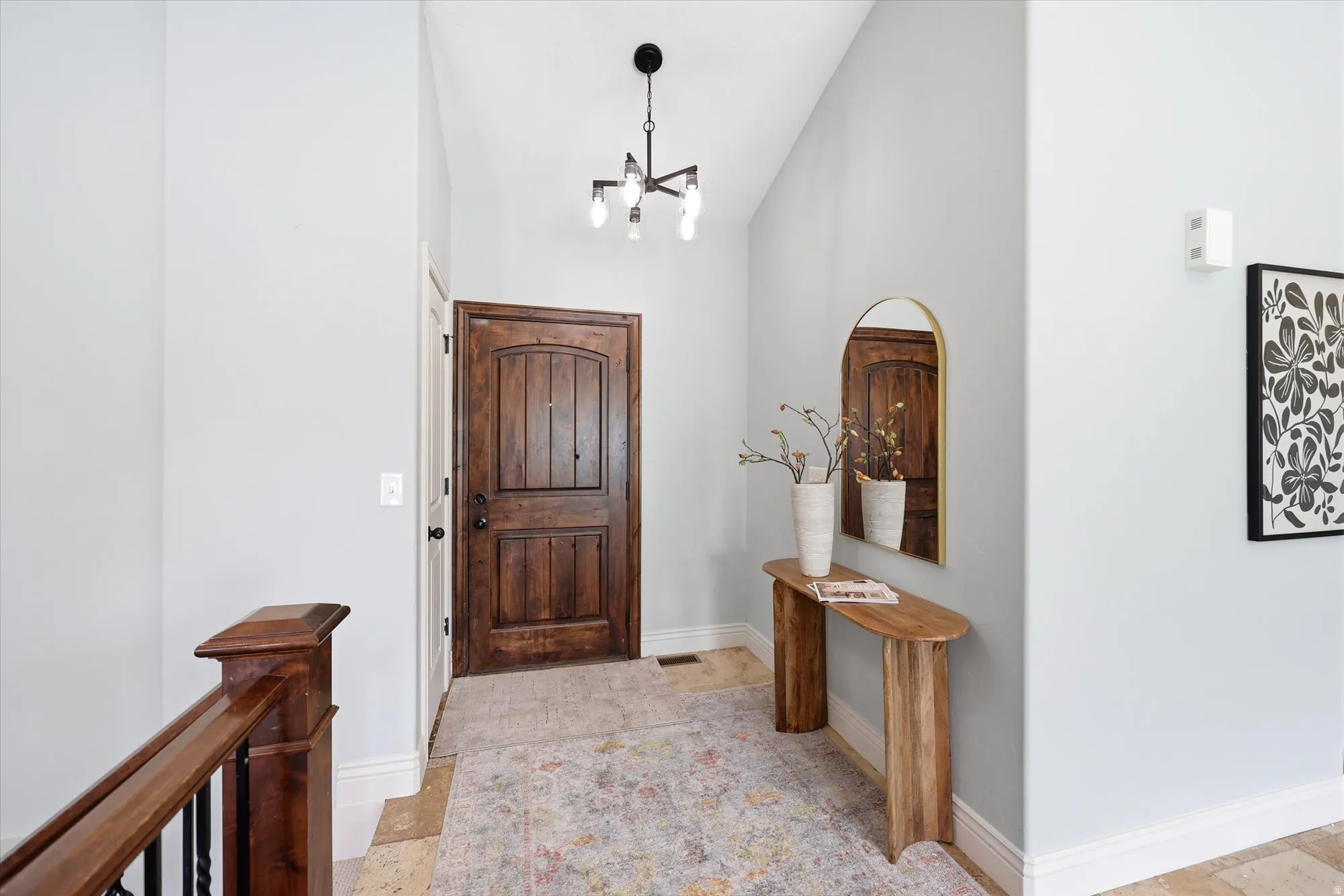 Foyer entrance featuring light stone finish flooring, vaulted ceiling, and suspended lighting