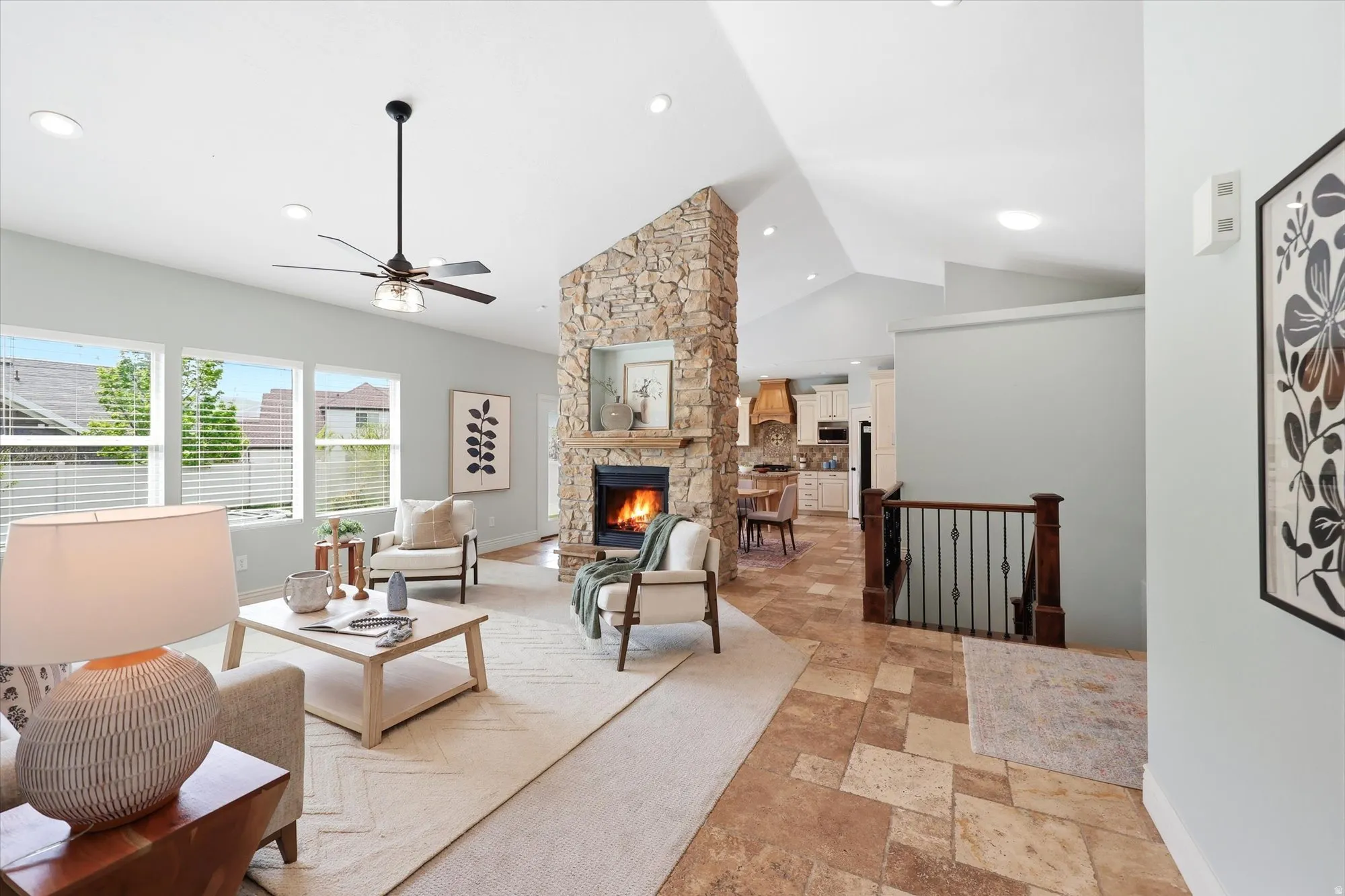 Living room featuring stone tile floors, a stone fireplace, a ceiling fan, and lofted ceiling