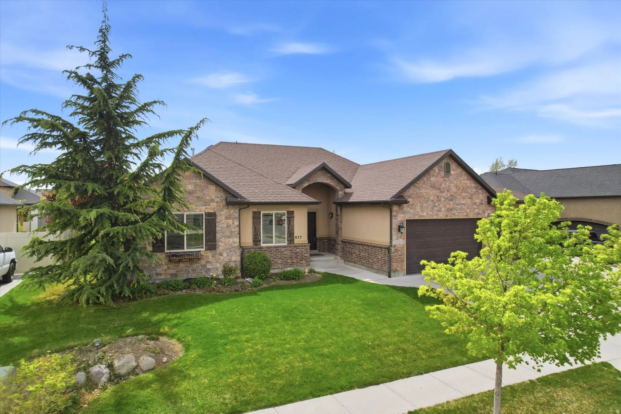 Craftsman house with a front lawn, an attached garage, stone siding, roof with shingles, and stucco siding