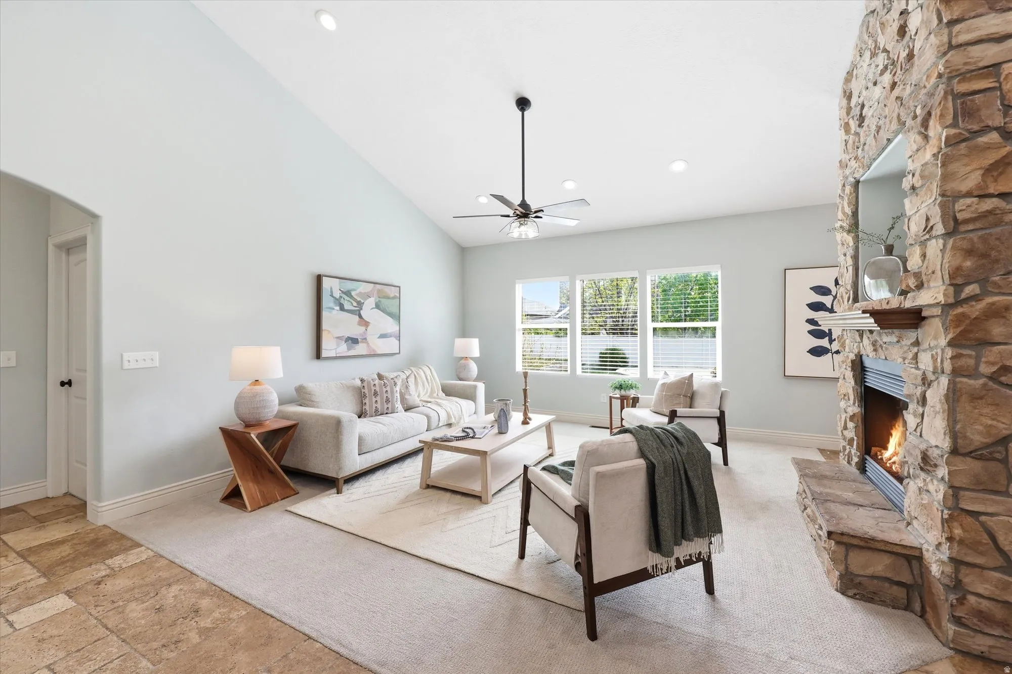 Living room featuring a stone fireplace, vaulted ceiling, stone tile floors, a ceiling fan, and recessed lighting