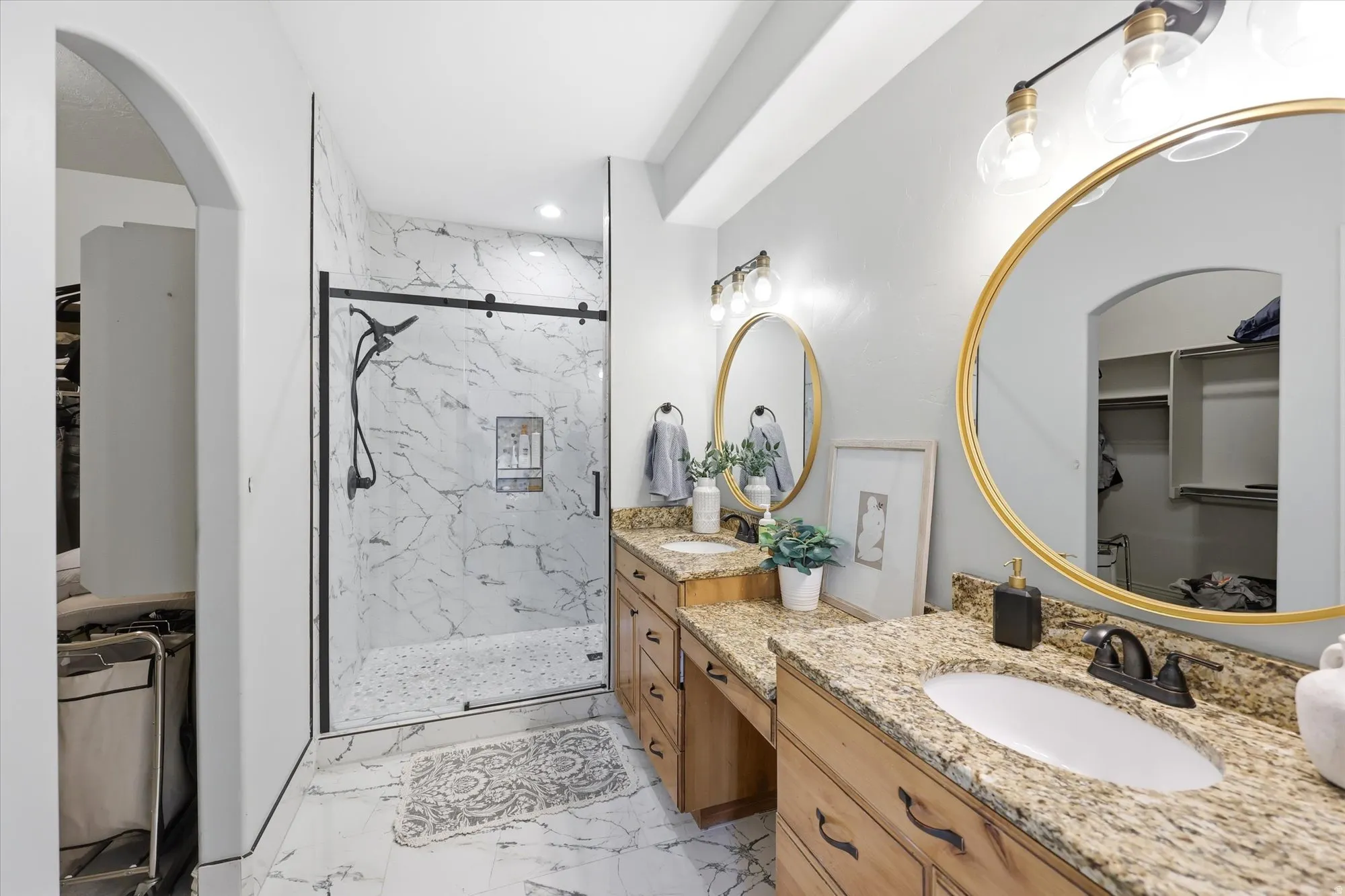 Full bathroom with a walk in closet, two vanities, a marble finish shower, and light marble finish flooring