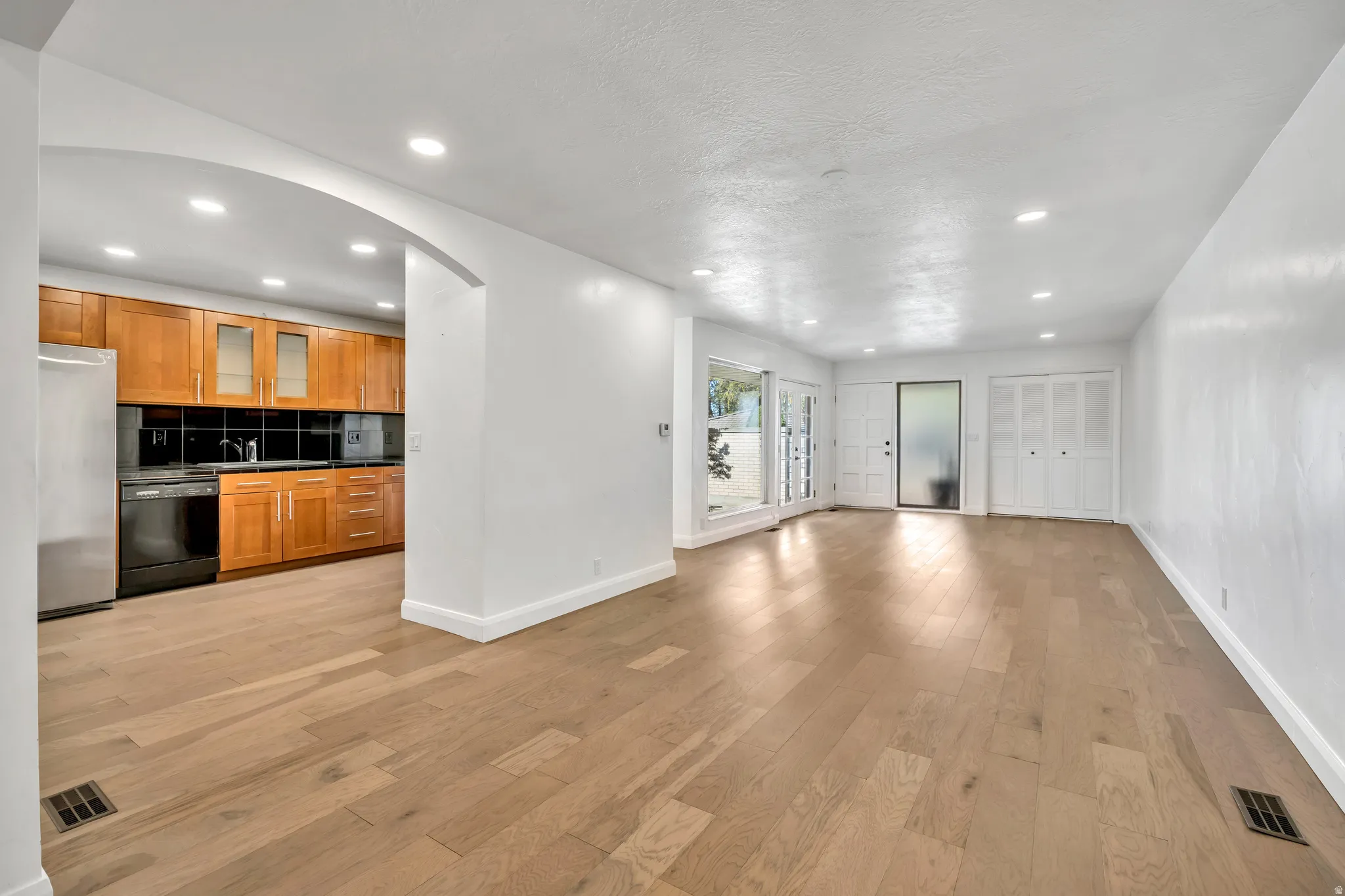 Kitchen featuring wood finish cabinets, arched walkways, freestanding refrigerator, light wood-style flooring, and black dishwasher