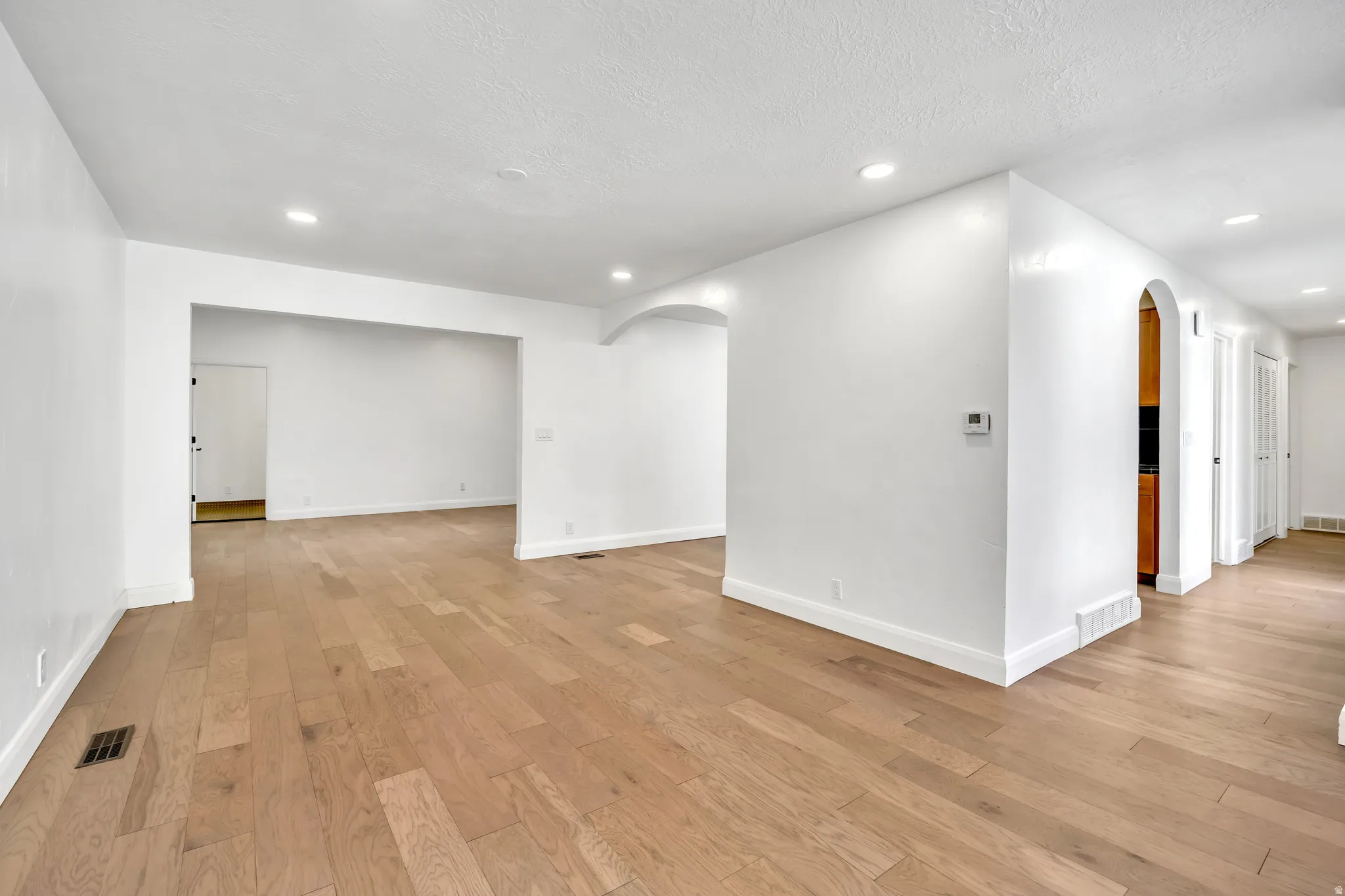 Unfurnished room featuring arched walkways, light wood-style flooring, and recessed lighting