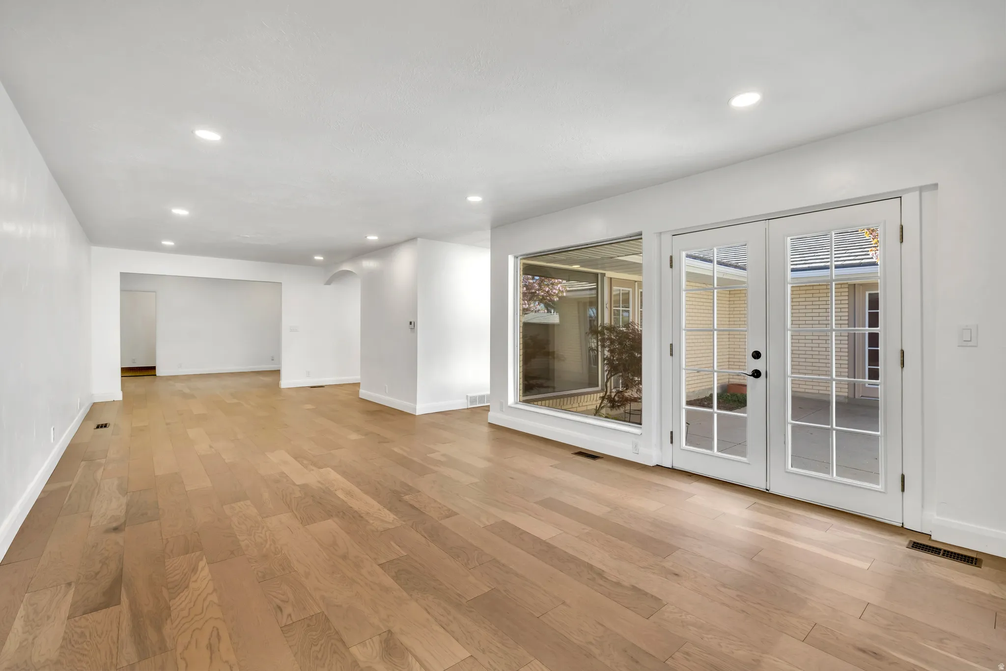 Spare room with arched walkways, light wood finished floors, recessed lighting, and french doors