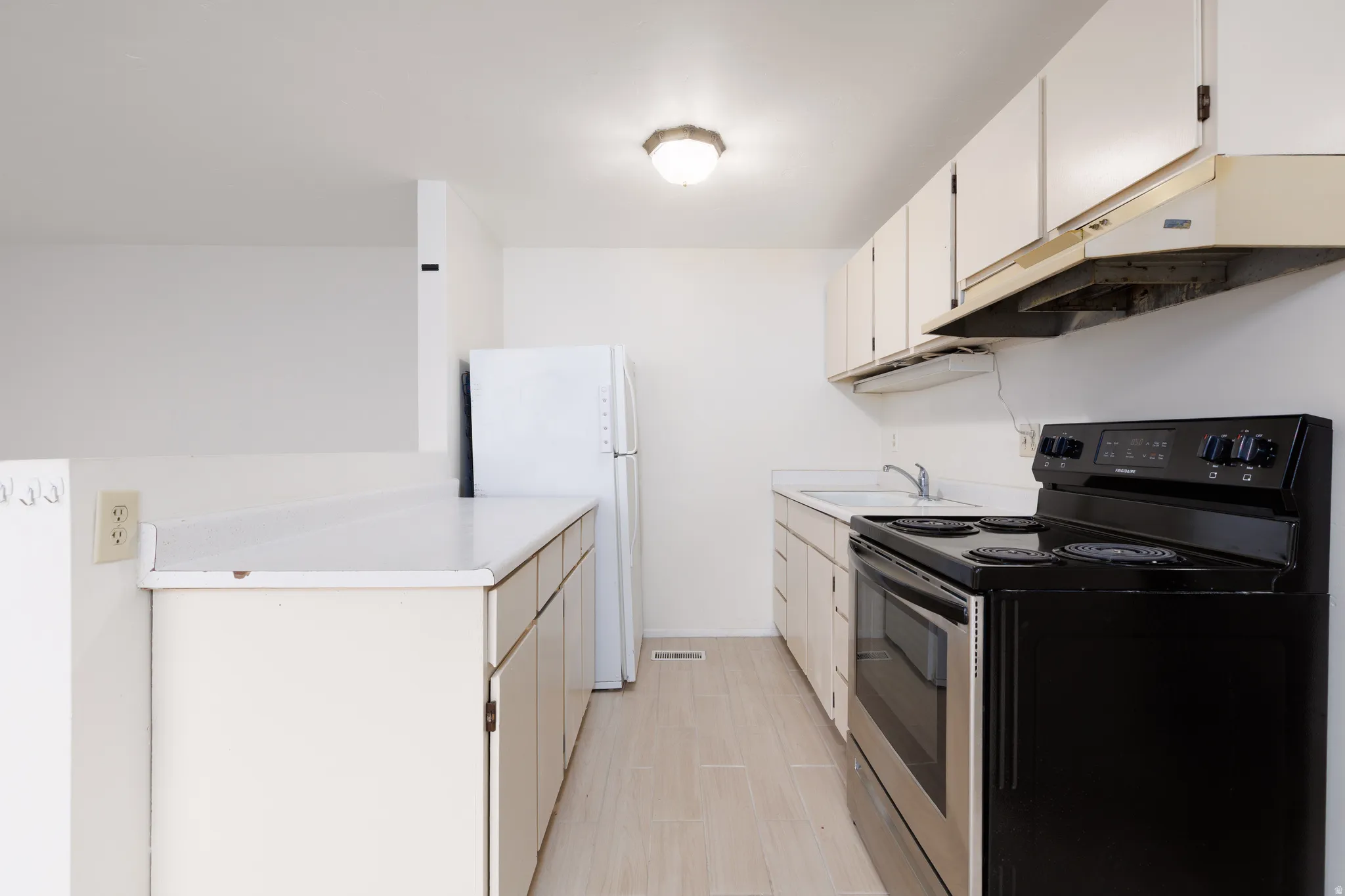 Kitchen with electric stove, light countertops, freestanding refrigerator, light wood-style floors, and white cabinetry