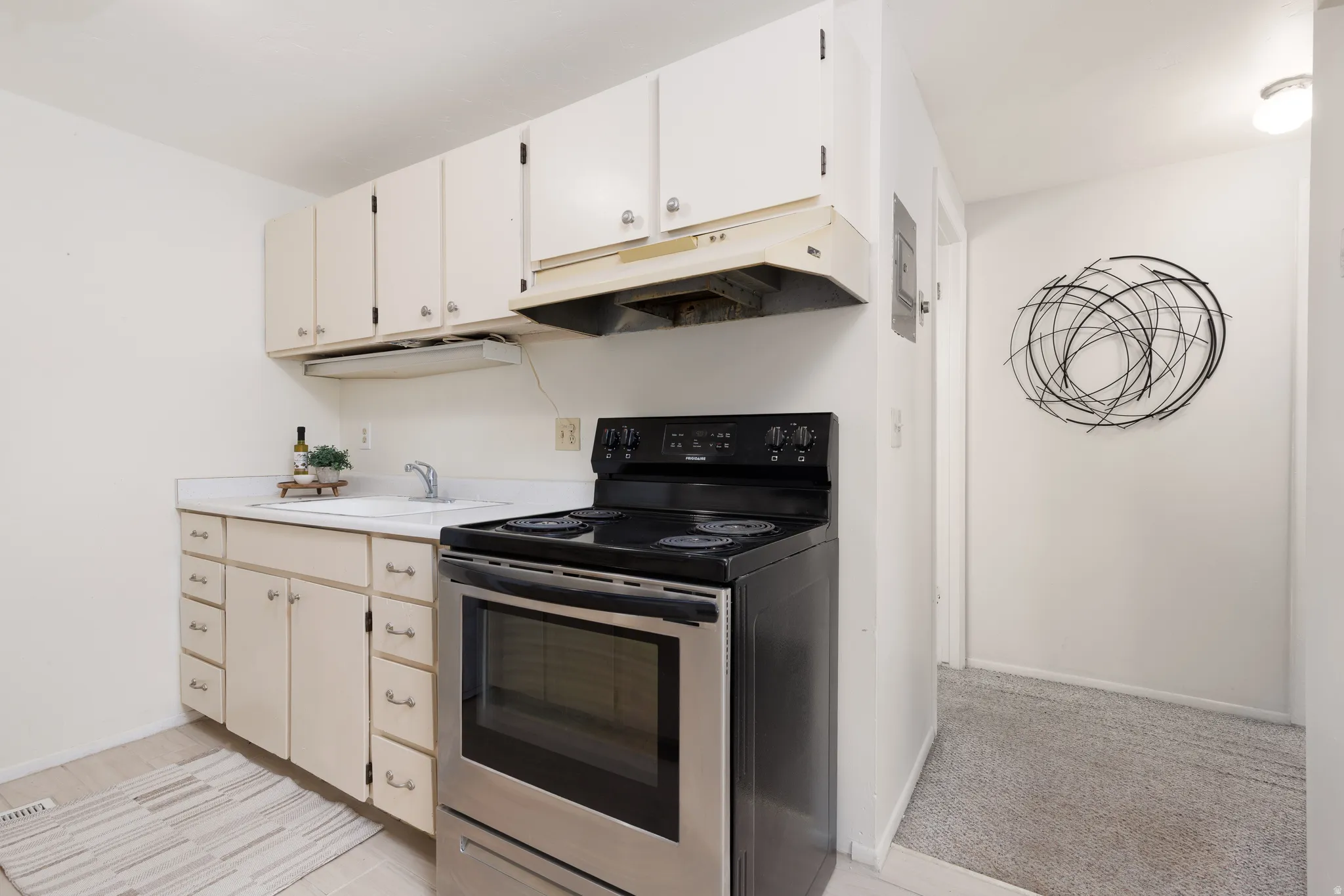 Kitchenette featuring white cabinetry, a stainless steel range, and a white countertop with an integrated sink