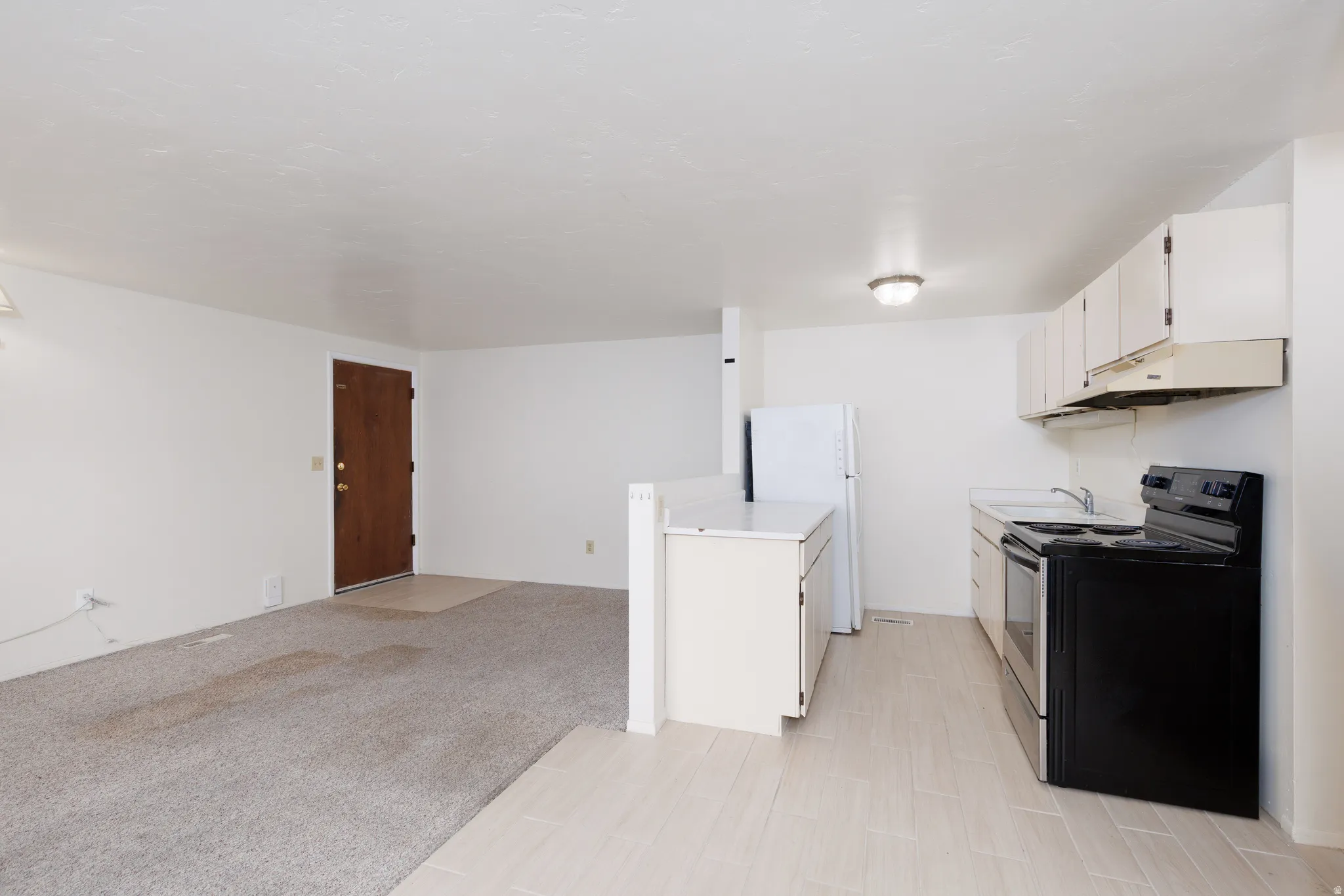 Kitchen with range with electric cooktop, light countertops, freestanding refrigerator, white cabinets, and light colored carpet