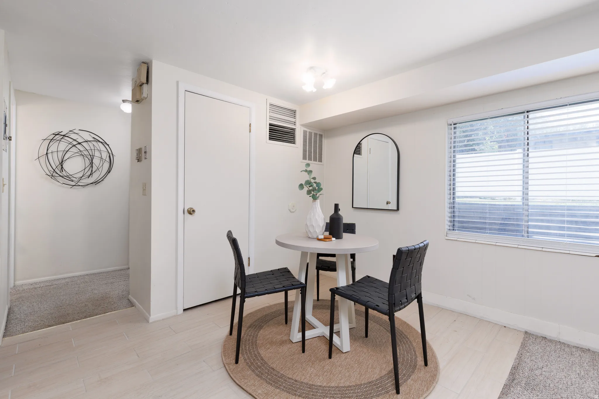 Open living area featuring wood-finish flooring, a bright window with blinds, and a white interior door