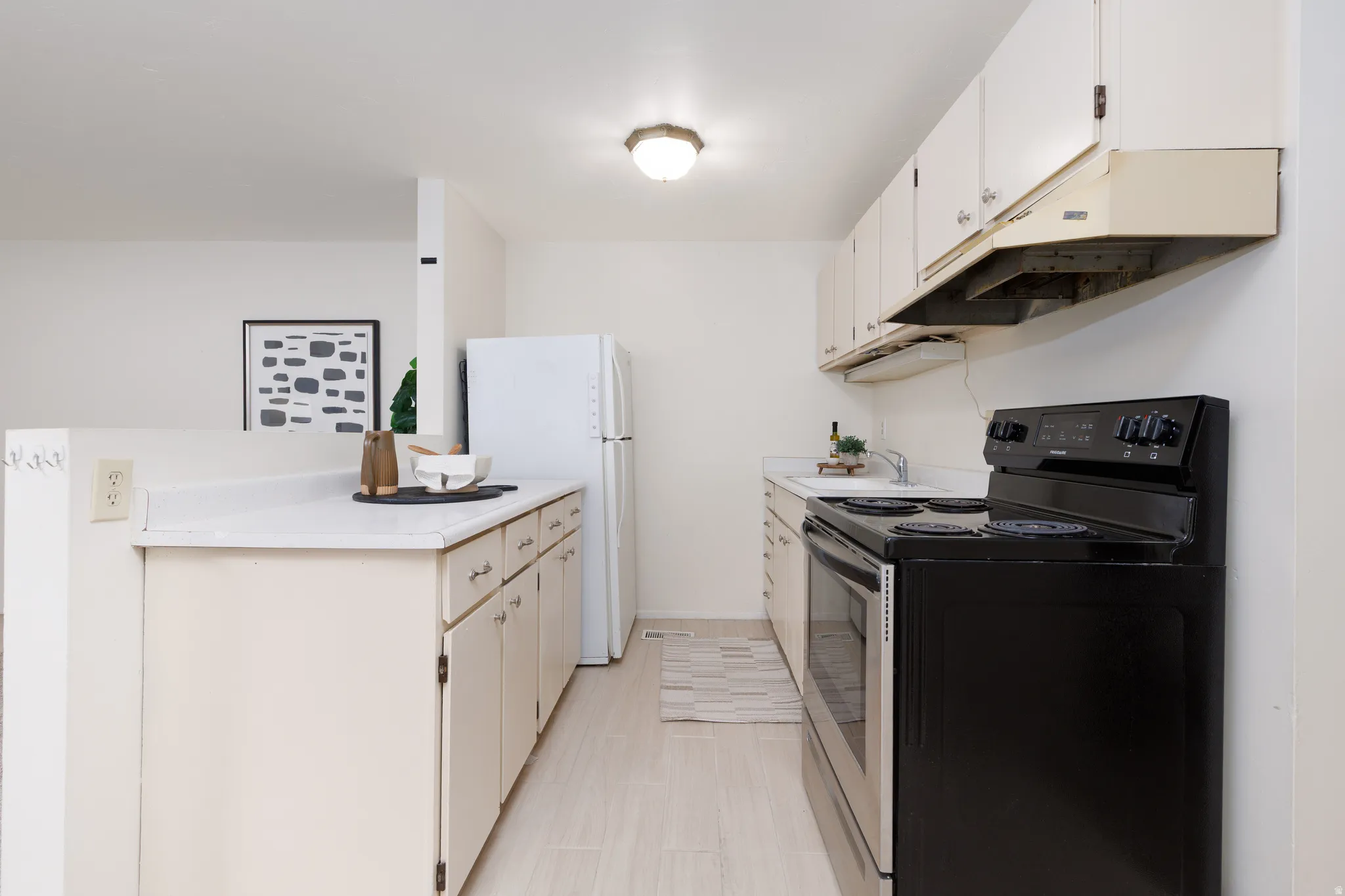 Kitchen featuring white cabinetry, light countertops, integrated white refrigerator, black electric range with coordinating hood, and wood-finish flooring
