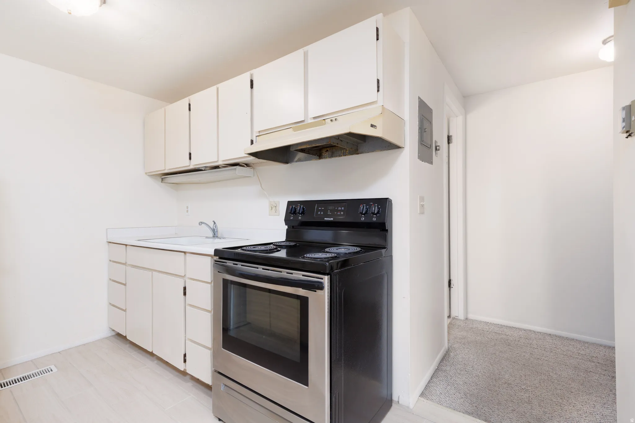 Kitchen with stainless steel electric range oven, light countertops, and white cabinetry