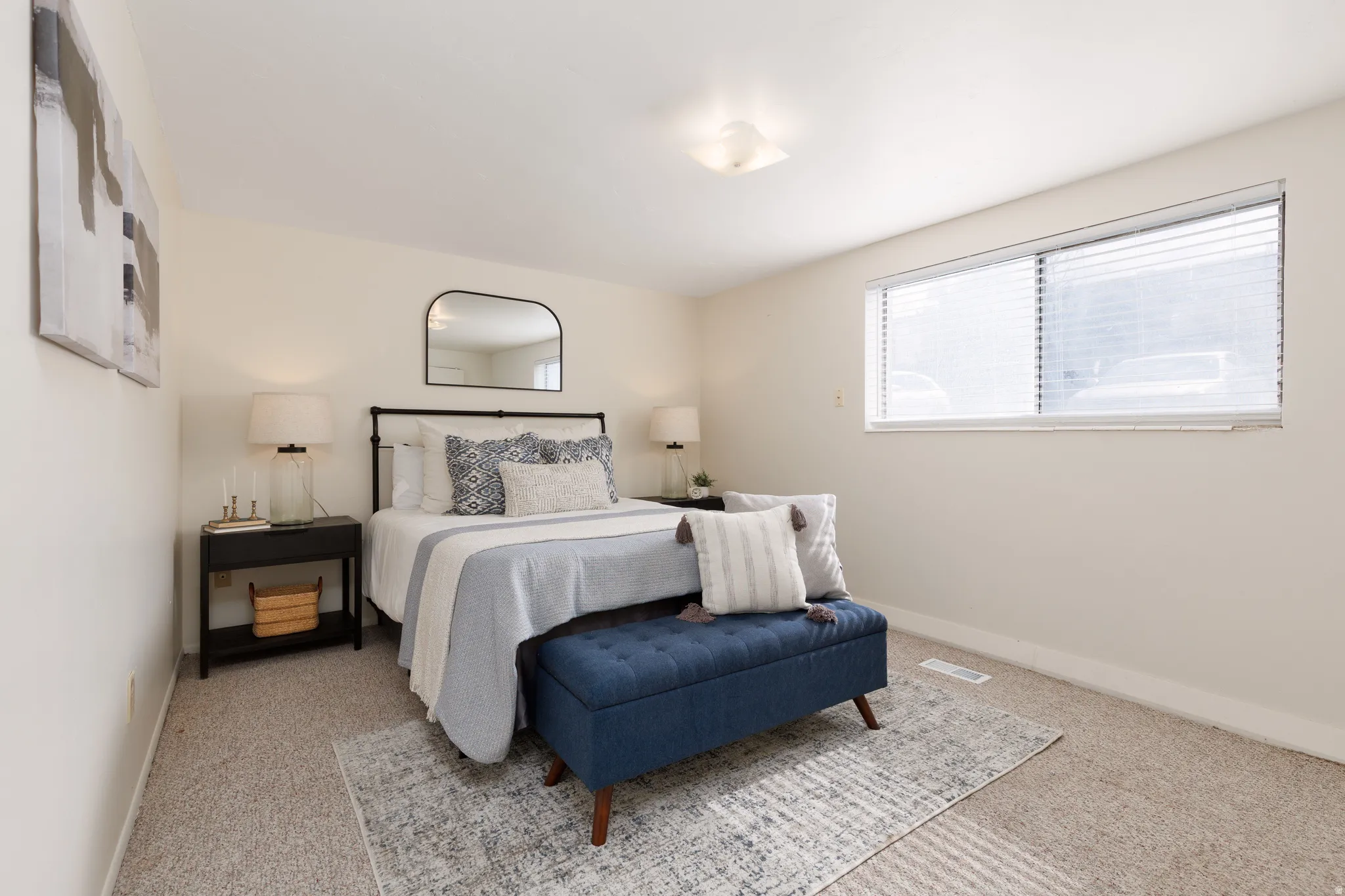 Carpeted bedroom featuring a large window with blinds, a ceiling-mounted light fixture, and neutral wall tones