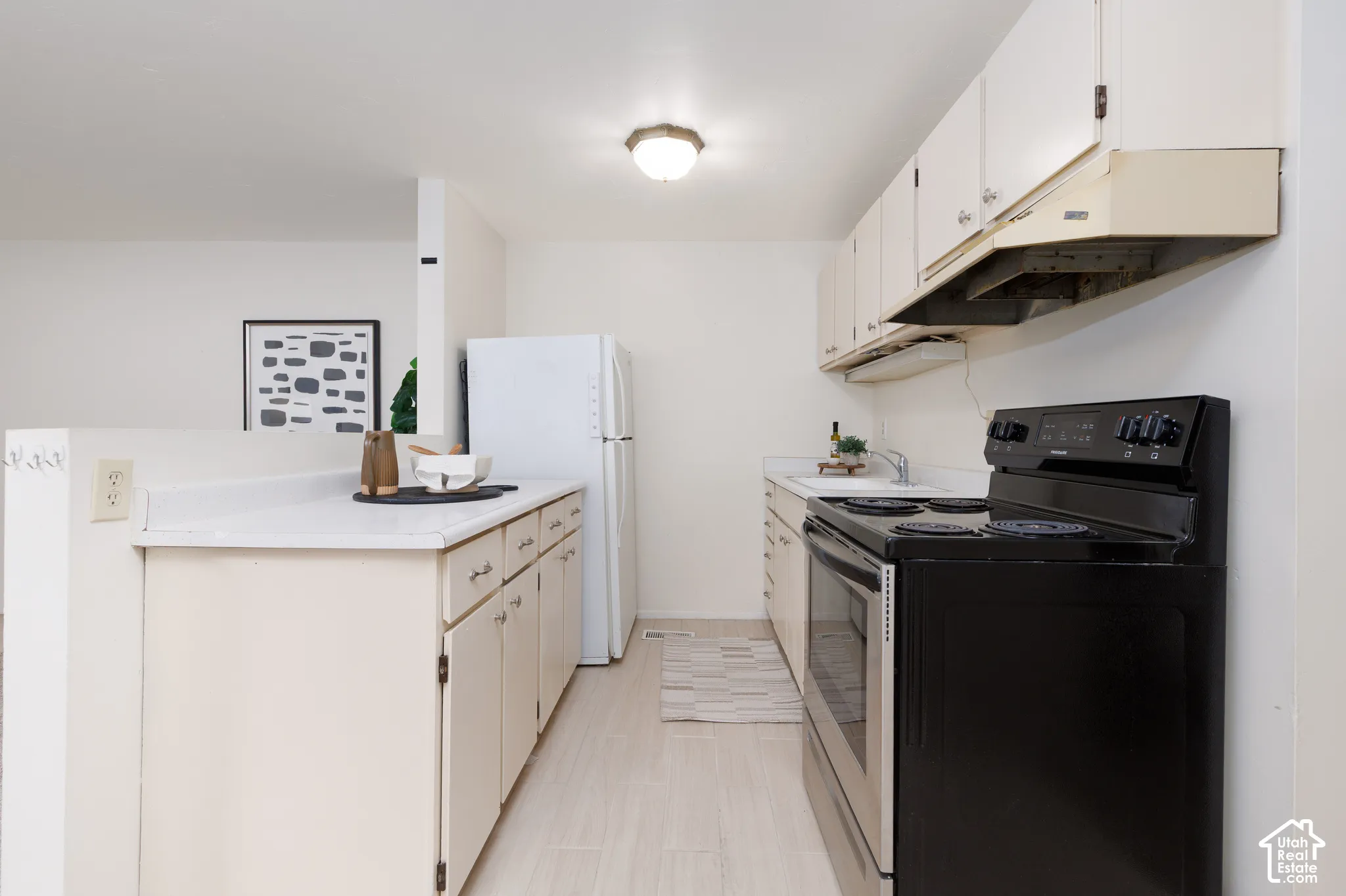 Kitchen featuring white cabinetry, light countertops, integrated white refrigerator, black electric range with coordinating hood, and wood-finish flooring
