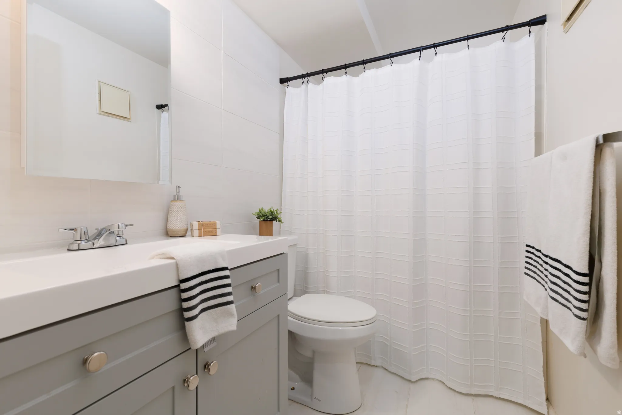 Bathroom featuring a gray vanity with chrome hardware, an integrated white sink, a chrome faucet, a wall-mounted mirror, and a shower with a black curtain rod