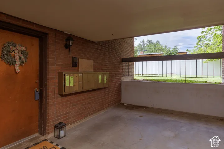 Covered entryway featuring a red brick wall, a solid entry door, built-in mailboxes, and a concrete patio