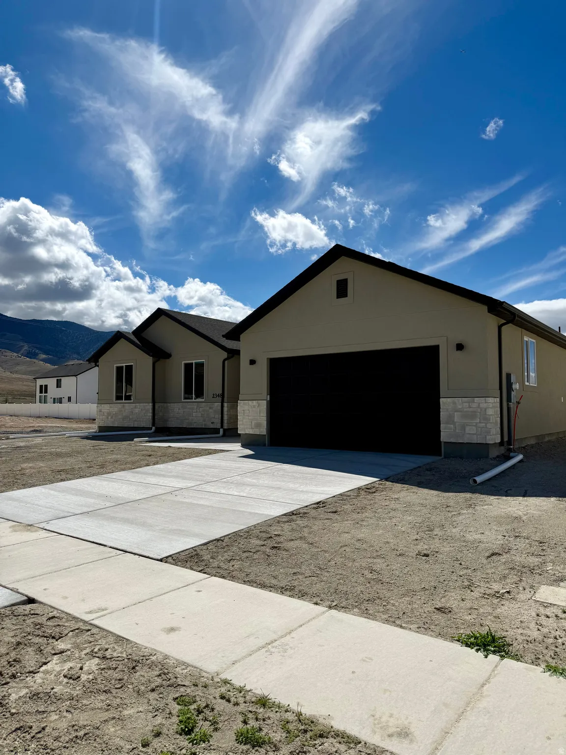 Ranch-style house featuring stone siding, concrete driveway, stucco siding, and a mountain view