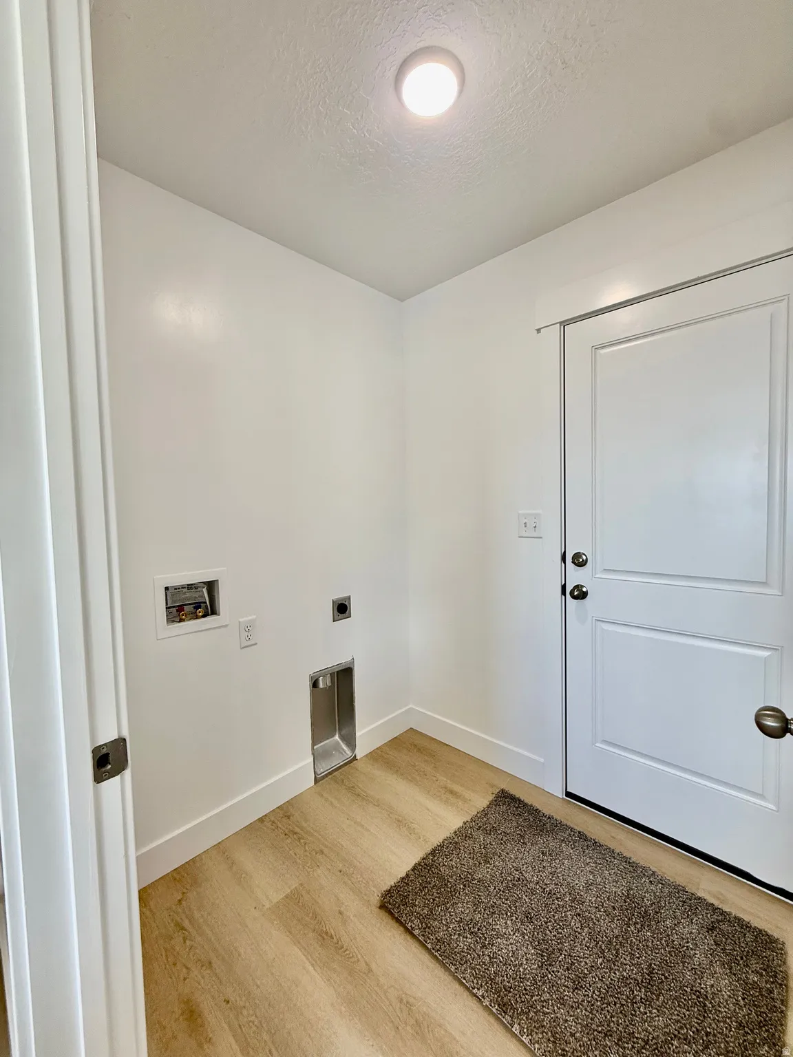 Laundry area with light wood finished floors, washer hookup, a textured ceiling, and electric dryer hookup