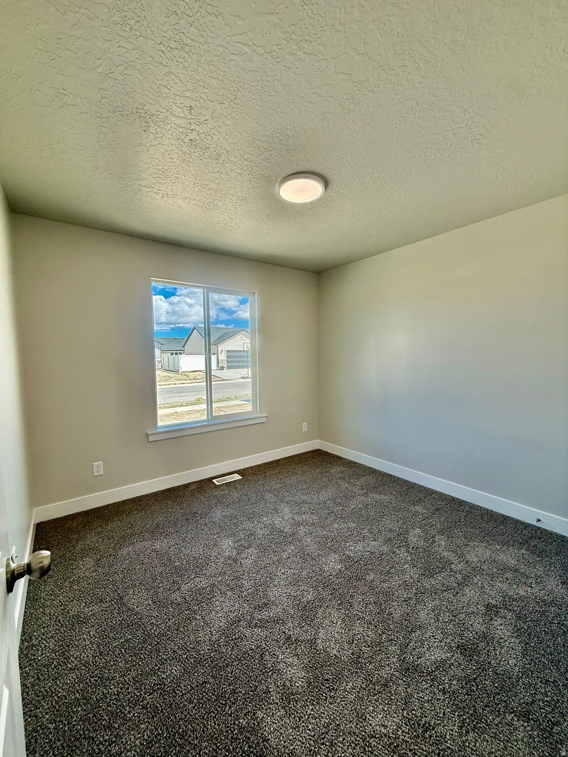 Empty room with a textured ceiling and dark carpet