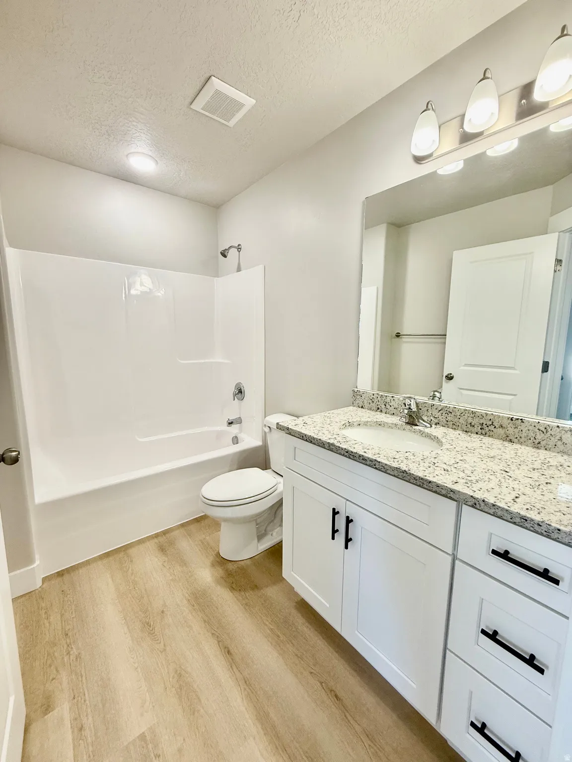 Full bath featuring a textured ceiling, vanity, light wood-type flooring, and shower / bathtub combination