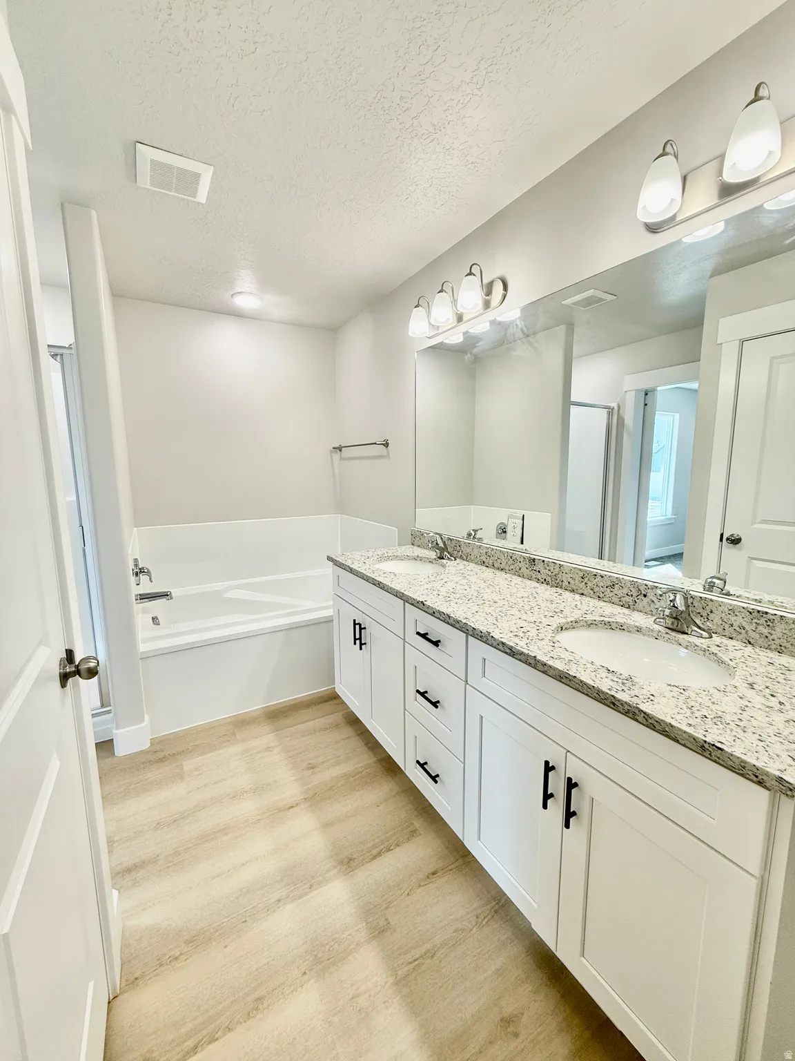 Full bath featuring double vanity, a bath, light wood-type flooring, a textured ceiling, and a stall shower
