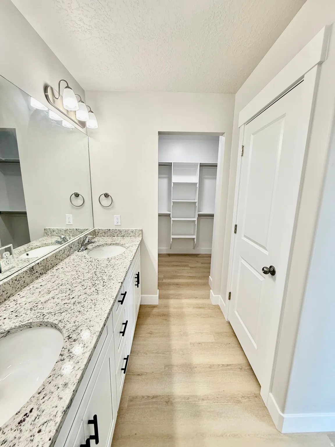 Bathroom featuring double vanity, a walk in closet, a textured ceiling, and light wood finished floors
