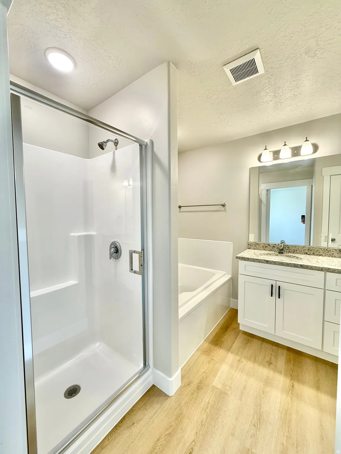 Bathroom featuring a textured ceiling, light wood finished floors, vanity, a stall shower, and a garden tub