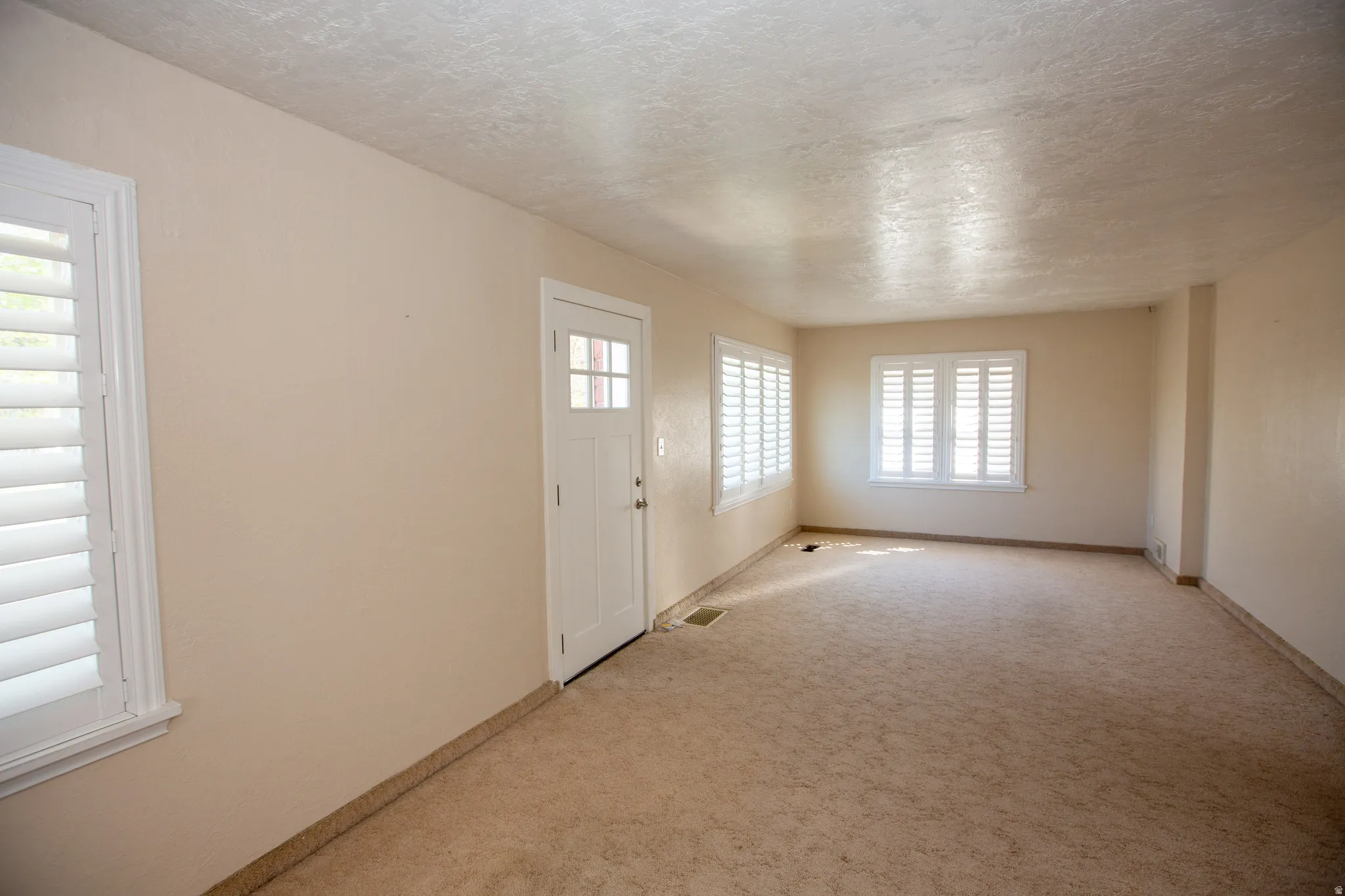 Large Family Room featuring light carpet and a textured ceiling, with plantation shutters