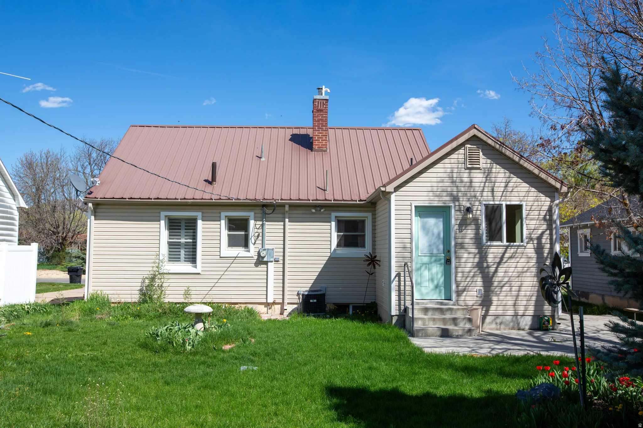 Back of property with entry steps, a lawn, a metal roof, and a chimney