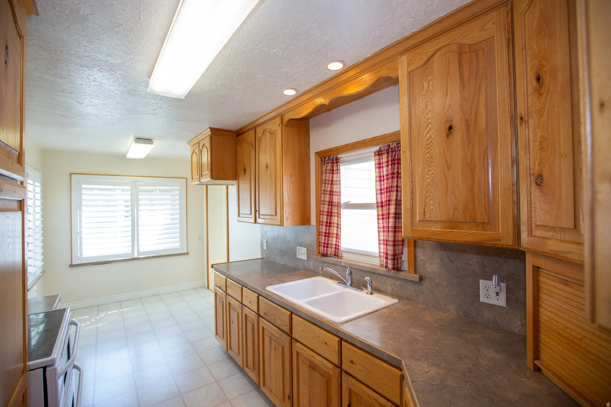 Kitchen with dark countertops, wood finish cabinets, backsplash, electric stove, and a textured ceiling