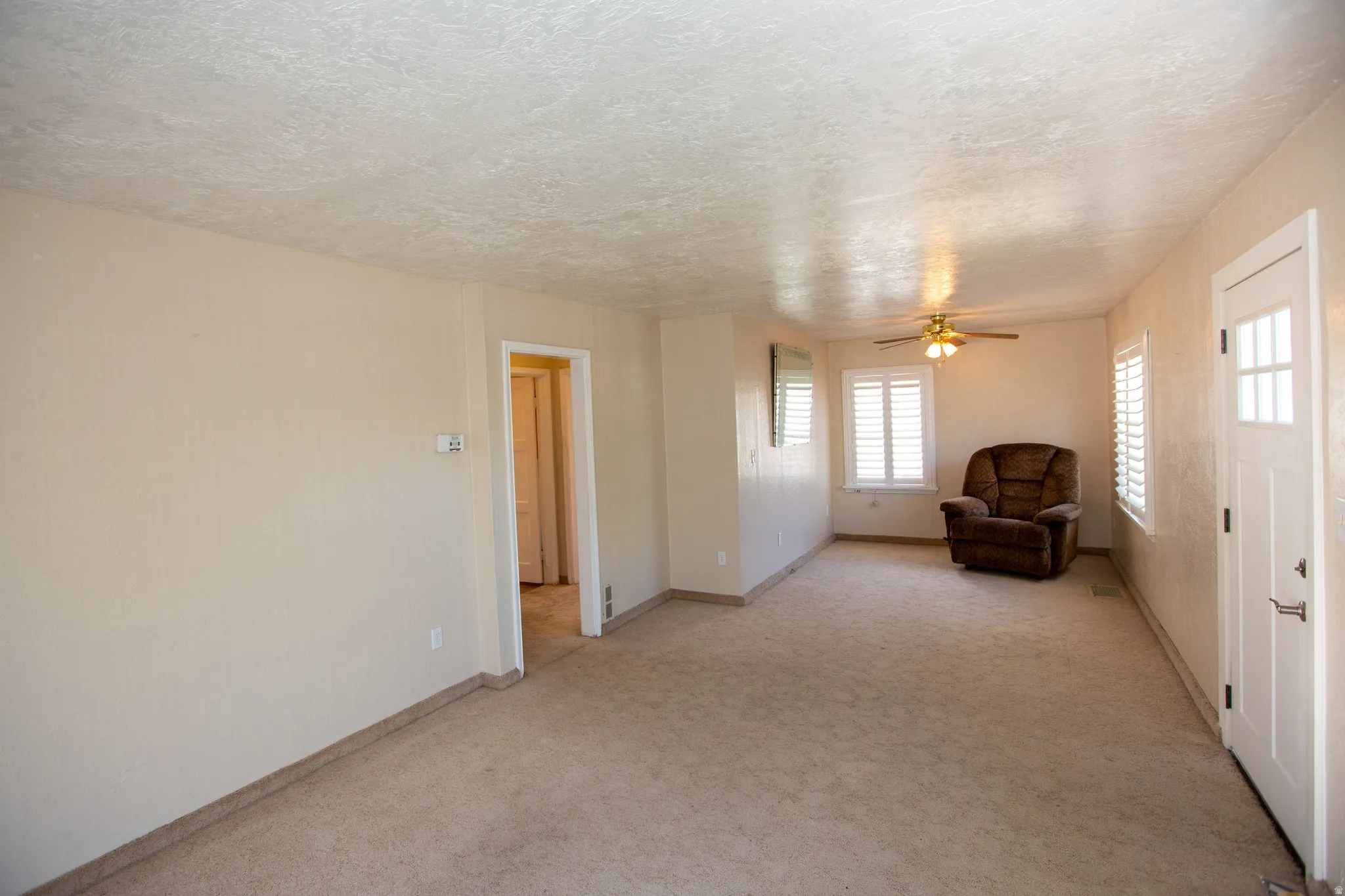Family room featuring light colored carpet, ceiling fan, and a textured ceiling, with plantation shutters