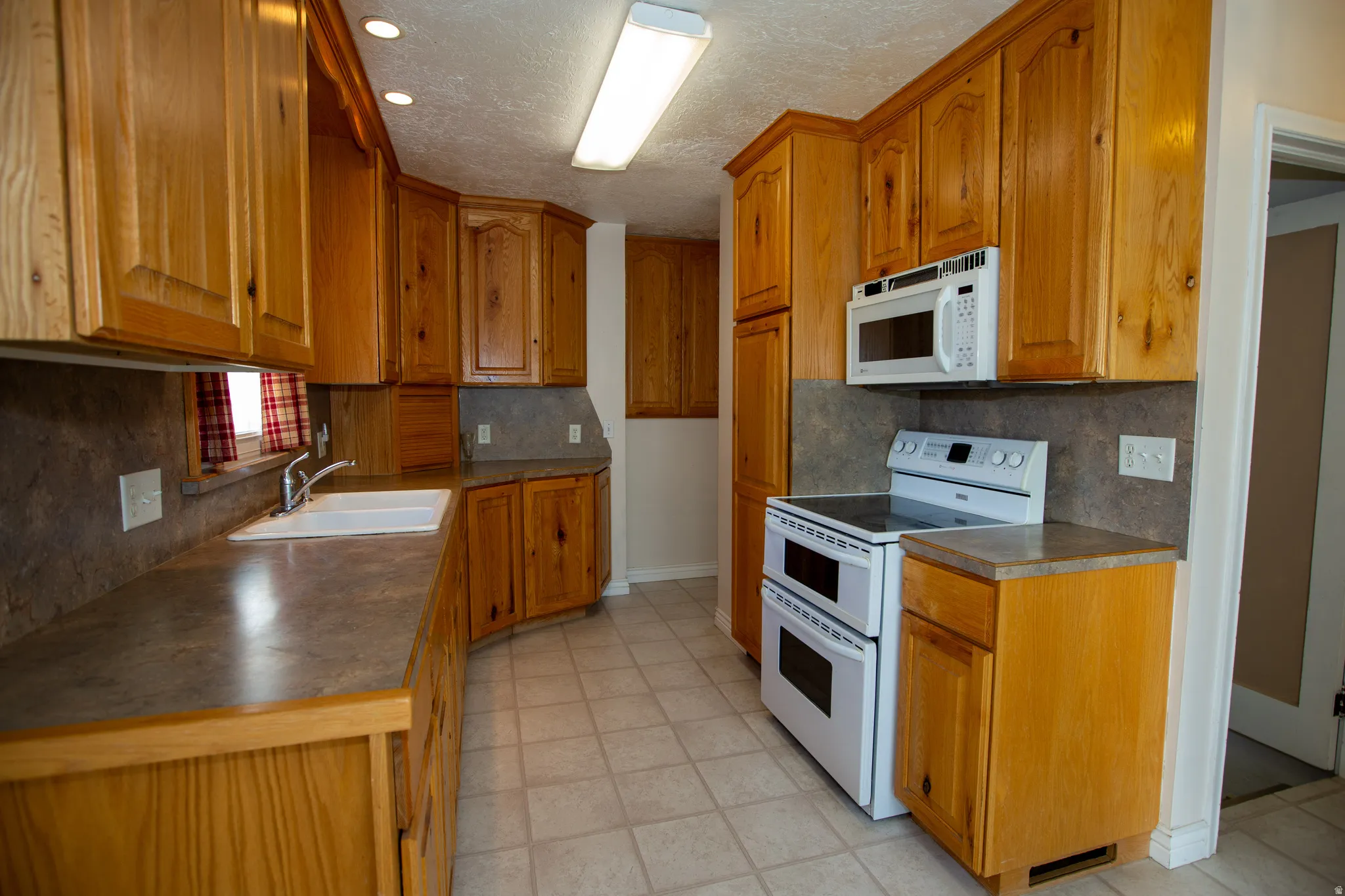 Kitchen with white appliances, wood finish cabinets, dark countertops, tasteful backsplash, and a textured ceiling