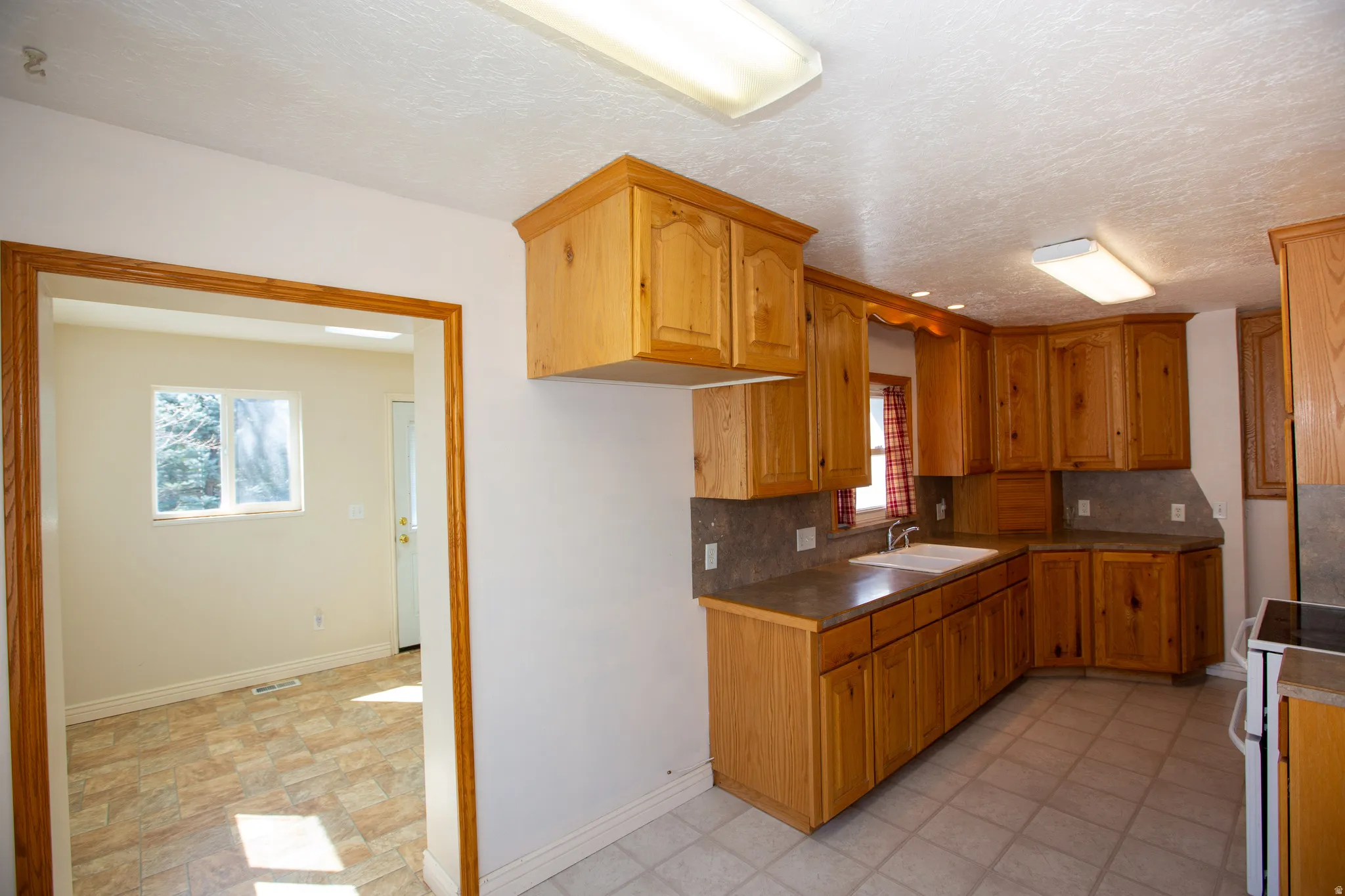 Kitchen featuring white electric range, tasteful backsplash, wood finish cabinets, a textured ceiling, and stone finish floors