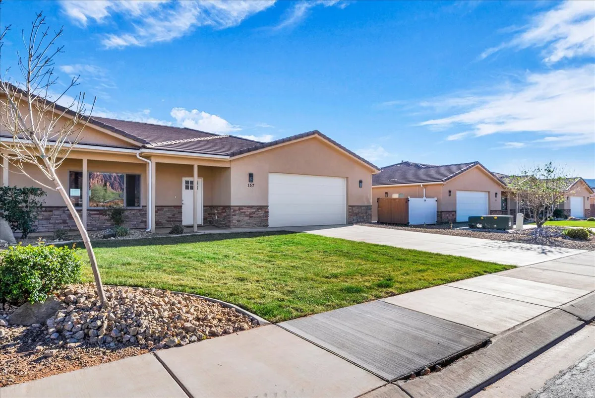 Single story home with stucco siding, stone siding, a garage, concrete driveway, and a porch