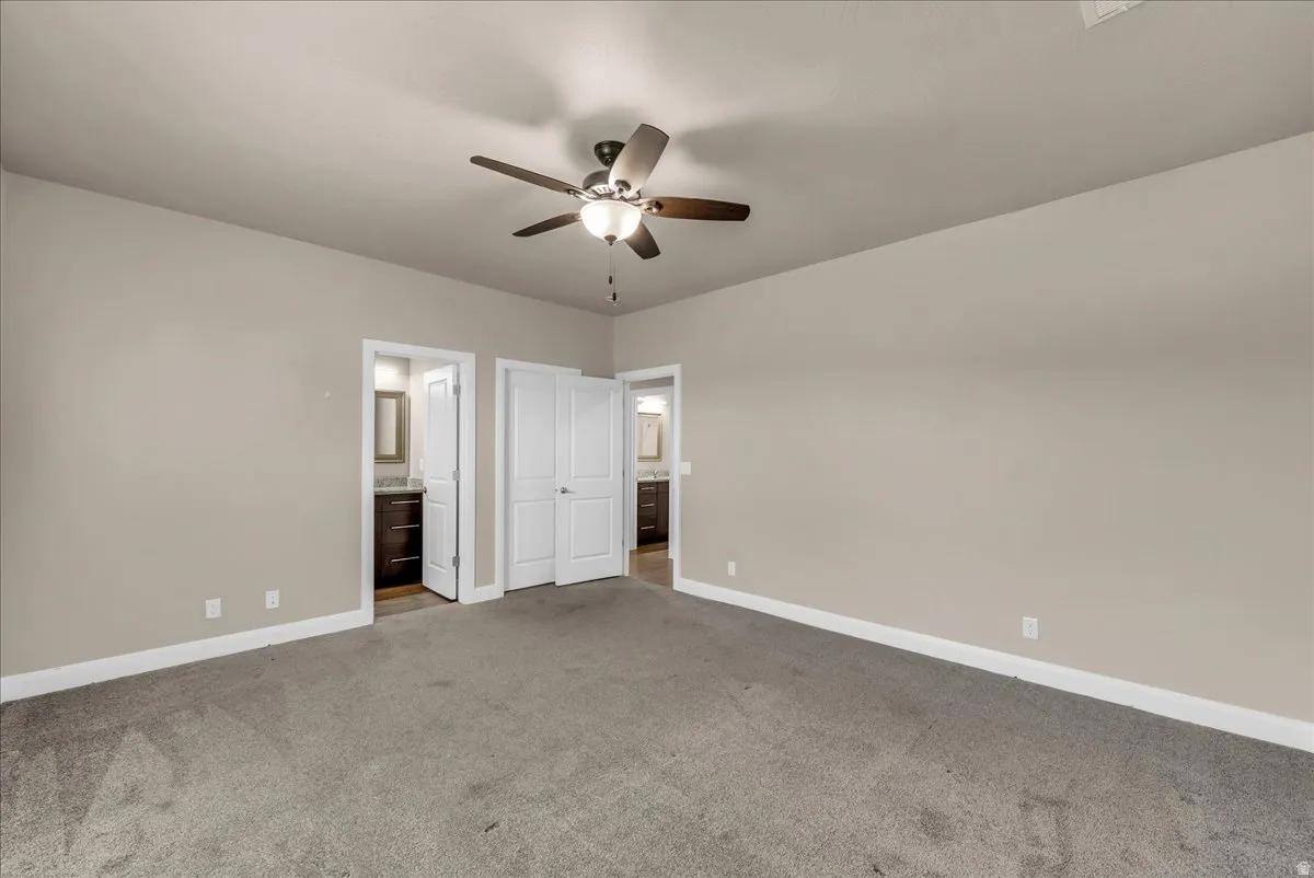 Unfurnished bedroom with connected bathroom, light carpet, and ceiling fan