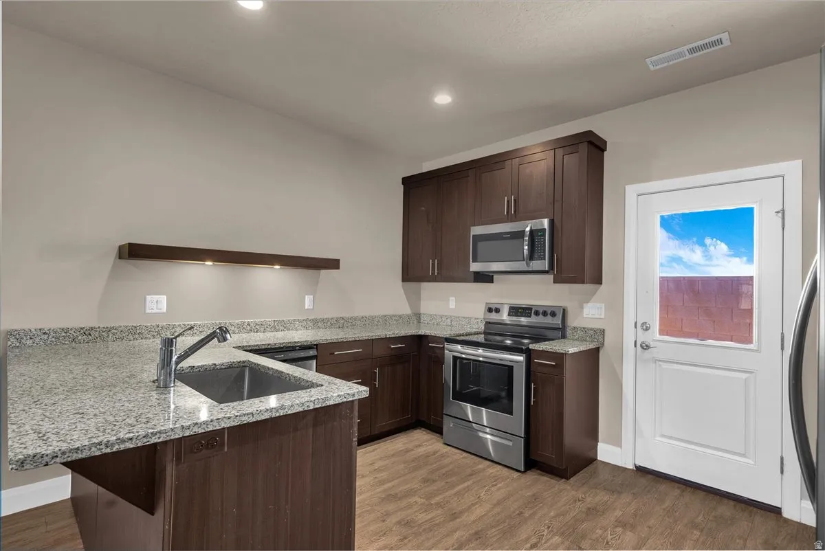 Kitchen featuring a peninsula, stainless steel appliances, light stone counters, dark wood finish cabinets, and recessed lighting