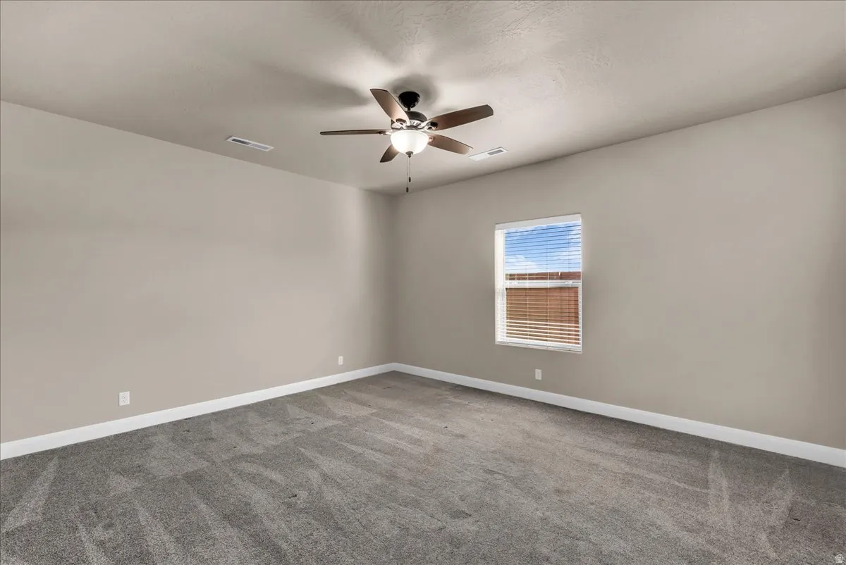 Carpeted empty room with ceiling fan and baseboards