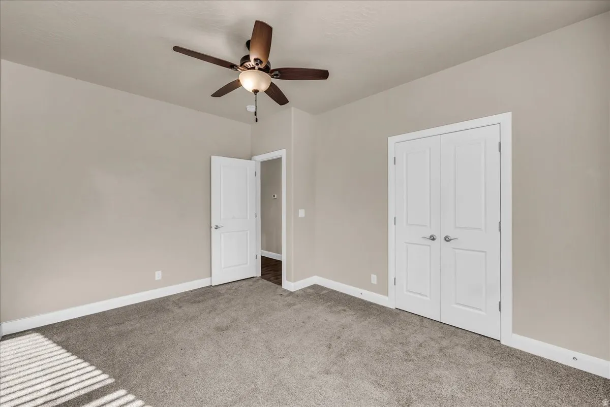 Unfurnished bedroom with light colored carpet, ceiling fan, and a closet